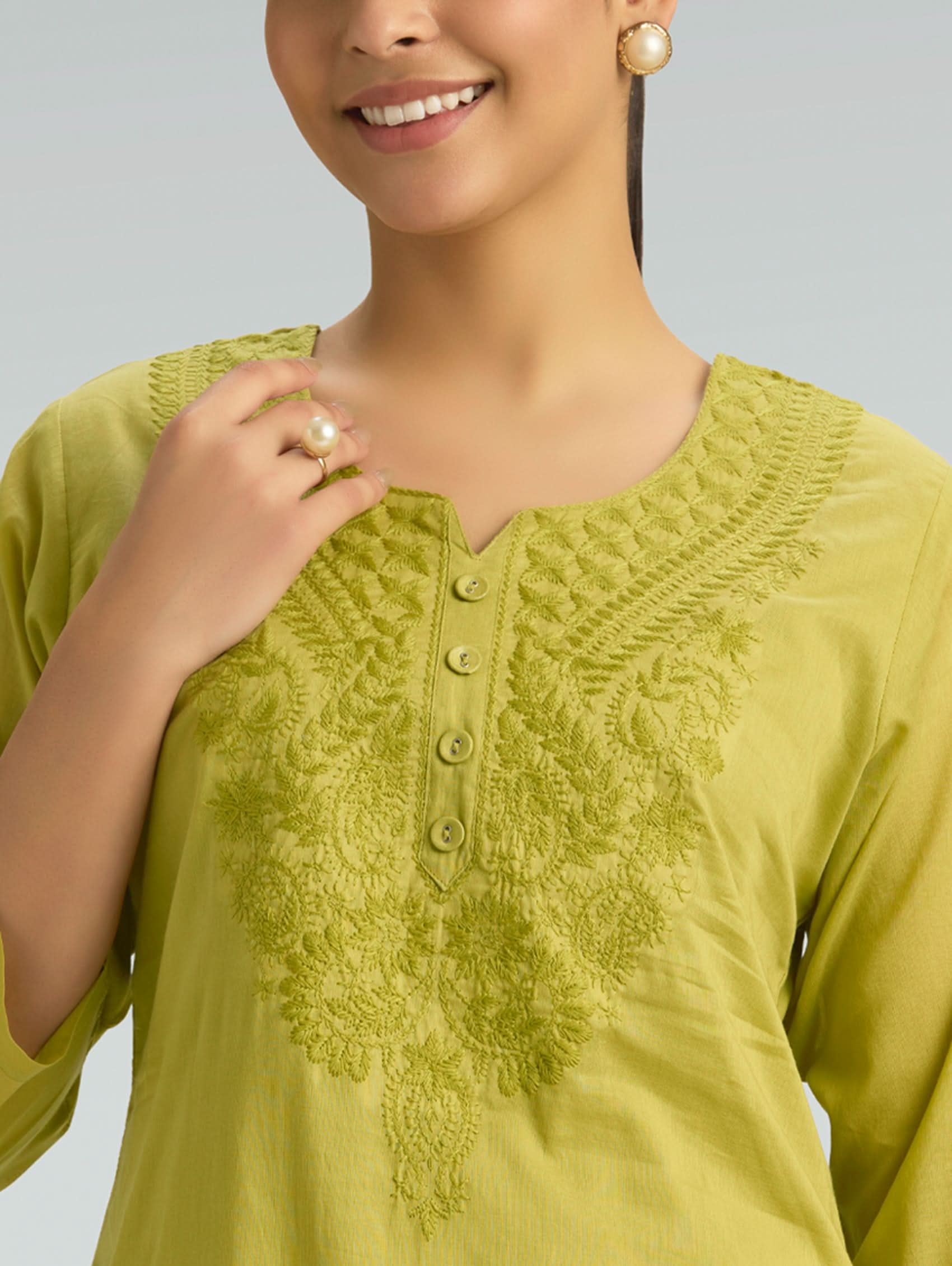 Woman wearing a green embroidered top against a gray background