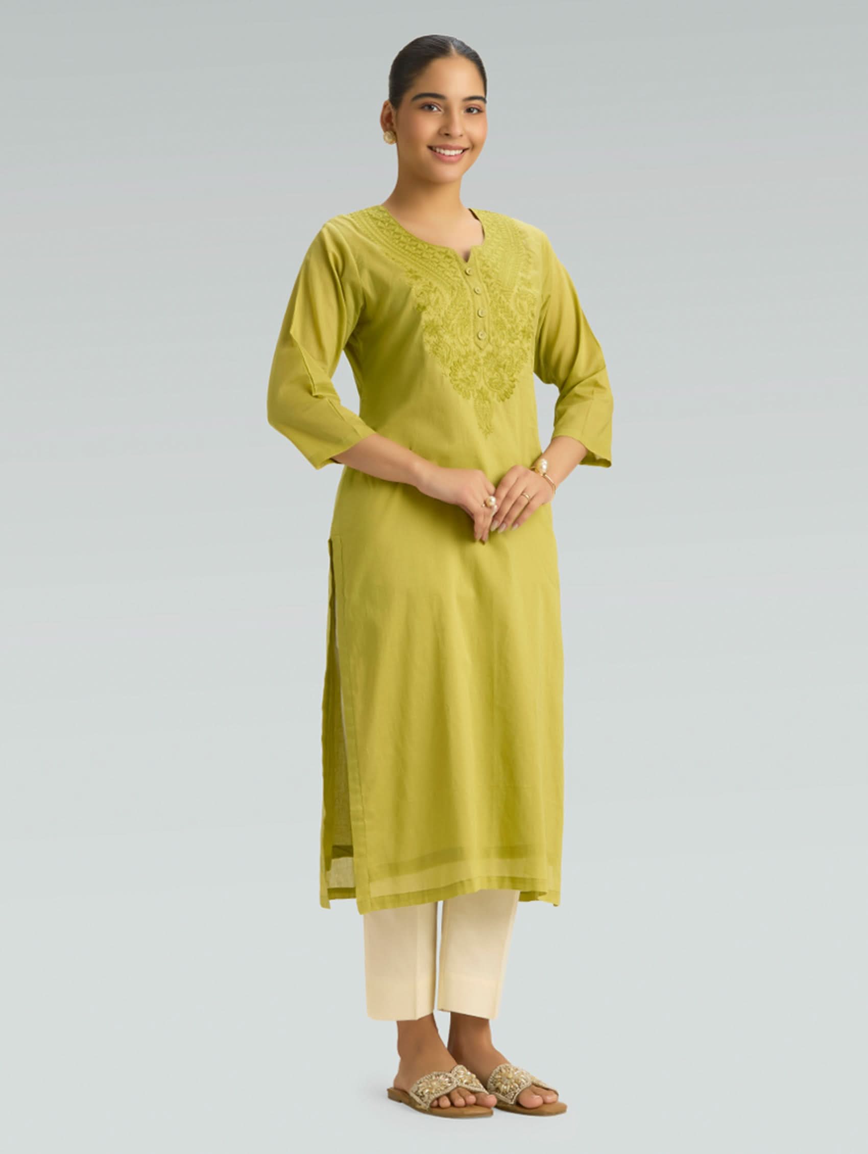 Woman wearing a green kurta with white pants on a gray background
