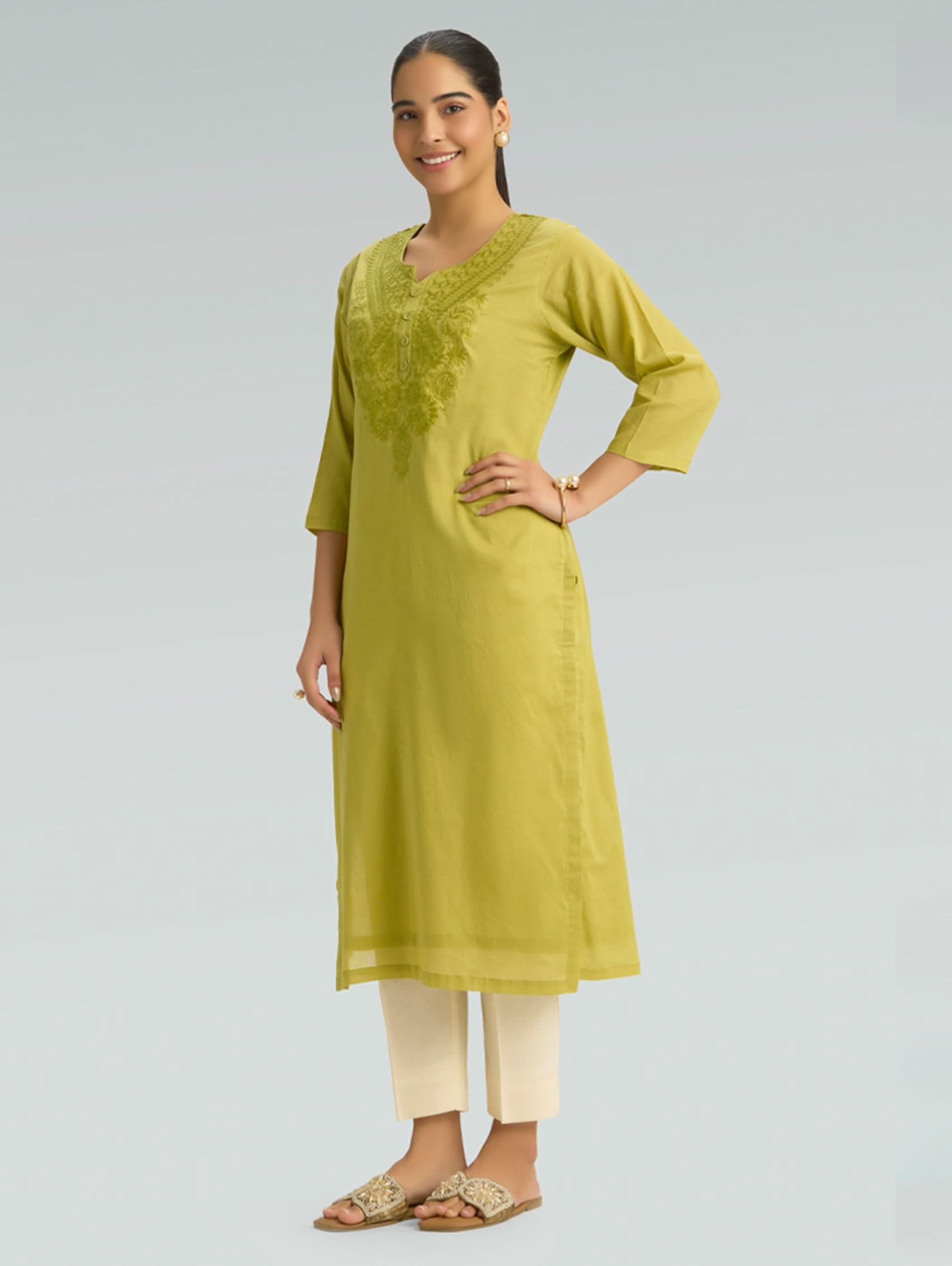 Woman wearing a green kurta with white pants on a gray background