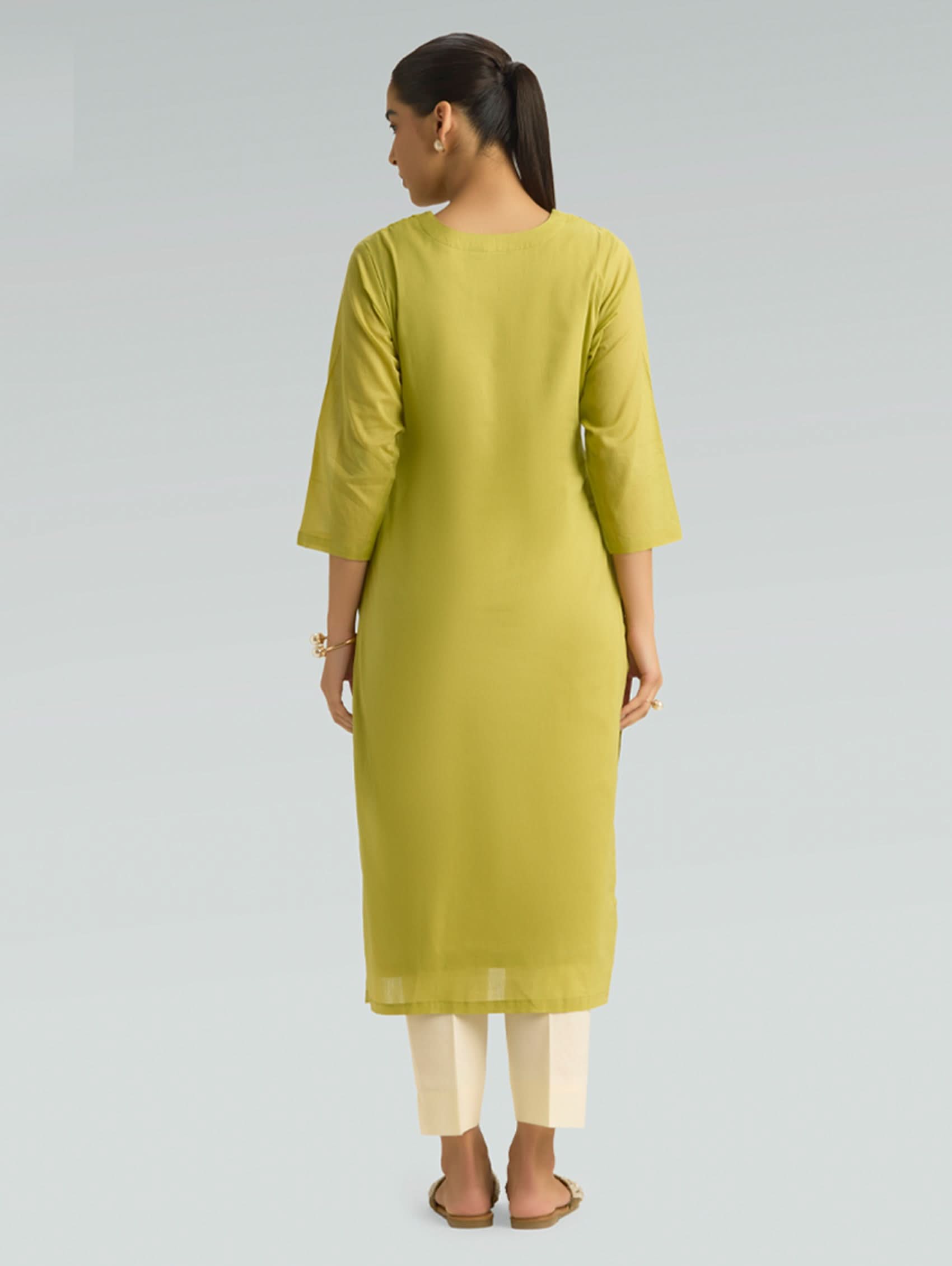 Woman wearing a green kurta with white pants on a gray background