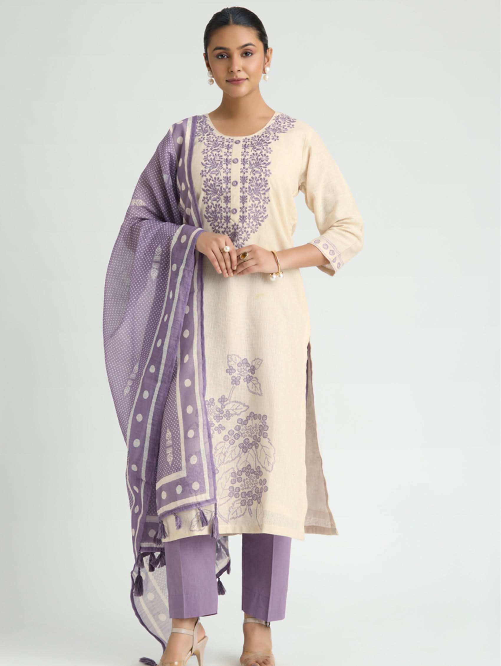 Woman wearing a cream kurta with purple embroidery, paired with a matching purple dupatta and pants on a light gray background.