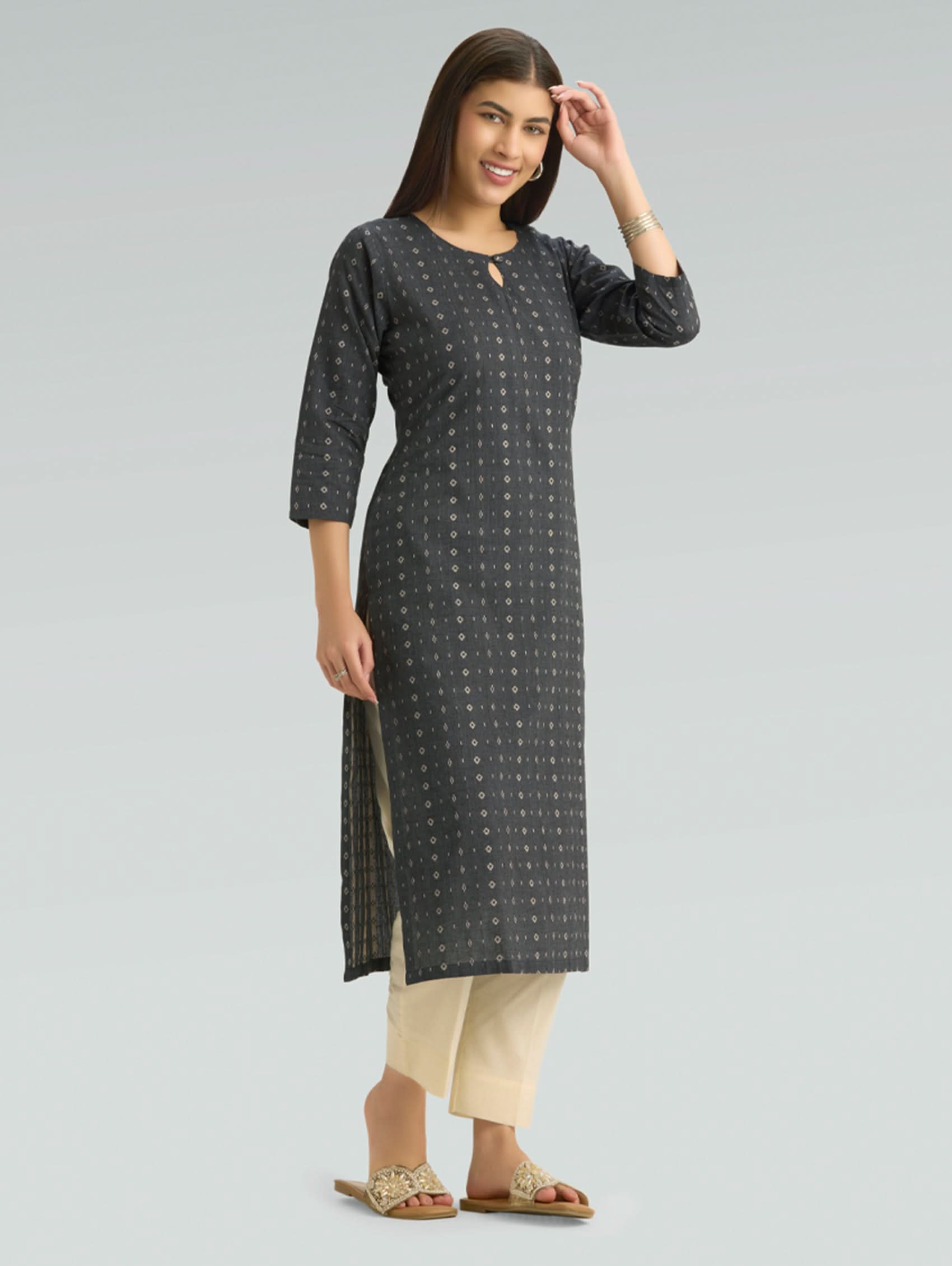 Woman wearing a black patterned kurta with beige pants and a round neckline on a grey background