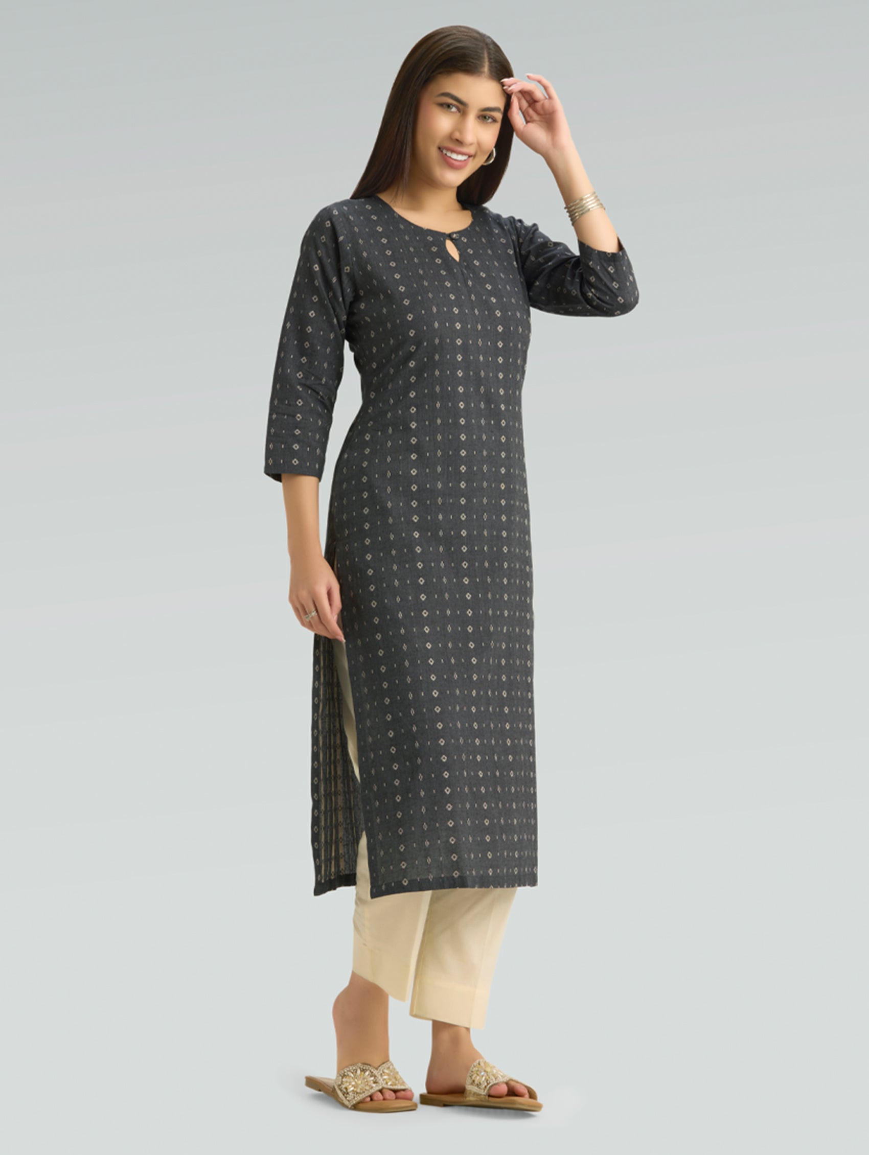 Woman wearing a black patterned kurta with beige pants and a round neckline on a grey background