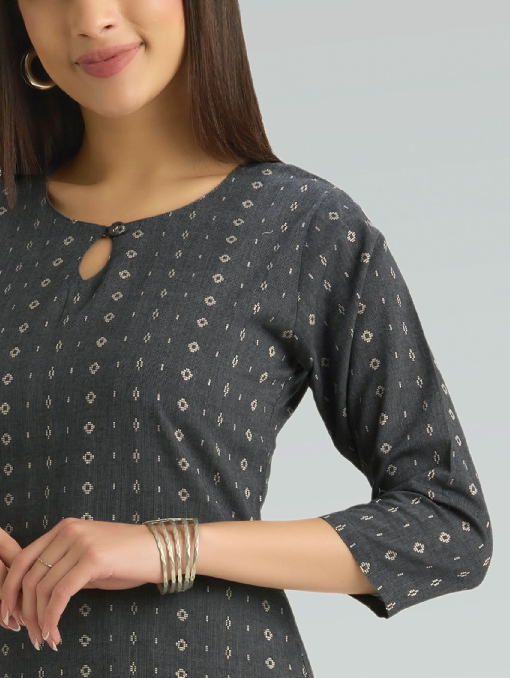 Woman wearing a dark grey patterned dress with long sleeves and keyhole neck on a light grey background