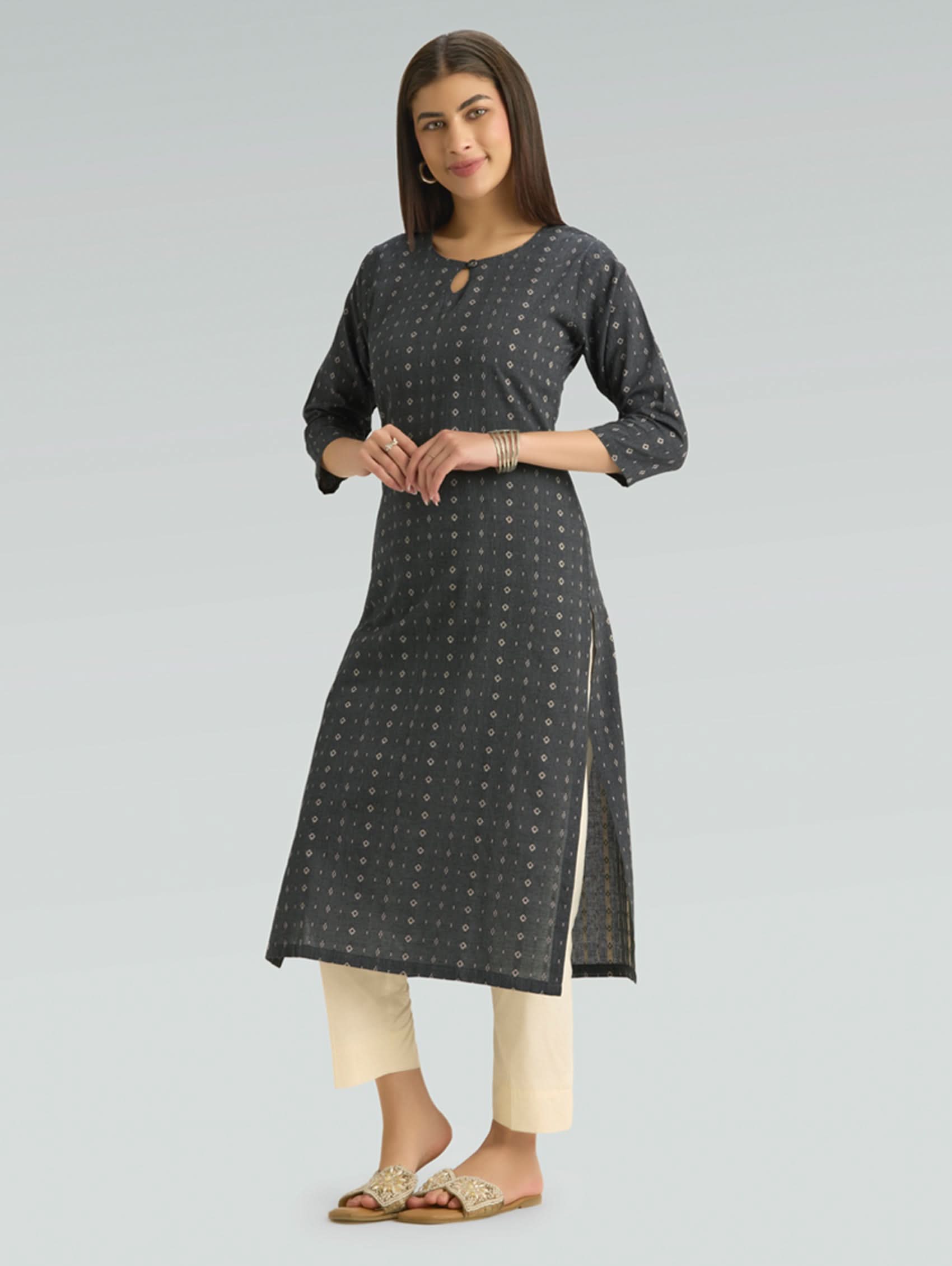Woman wearing a dark gray patterned kurta with white pants on a light gray background