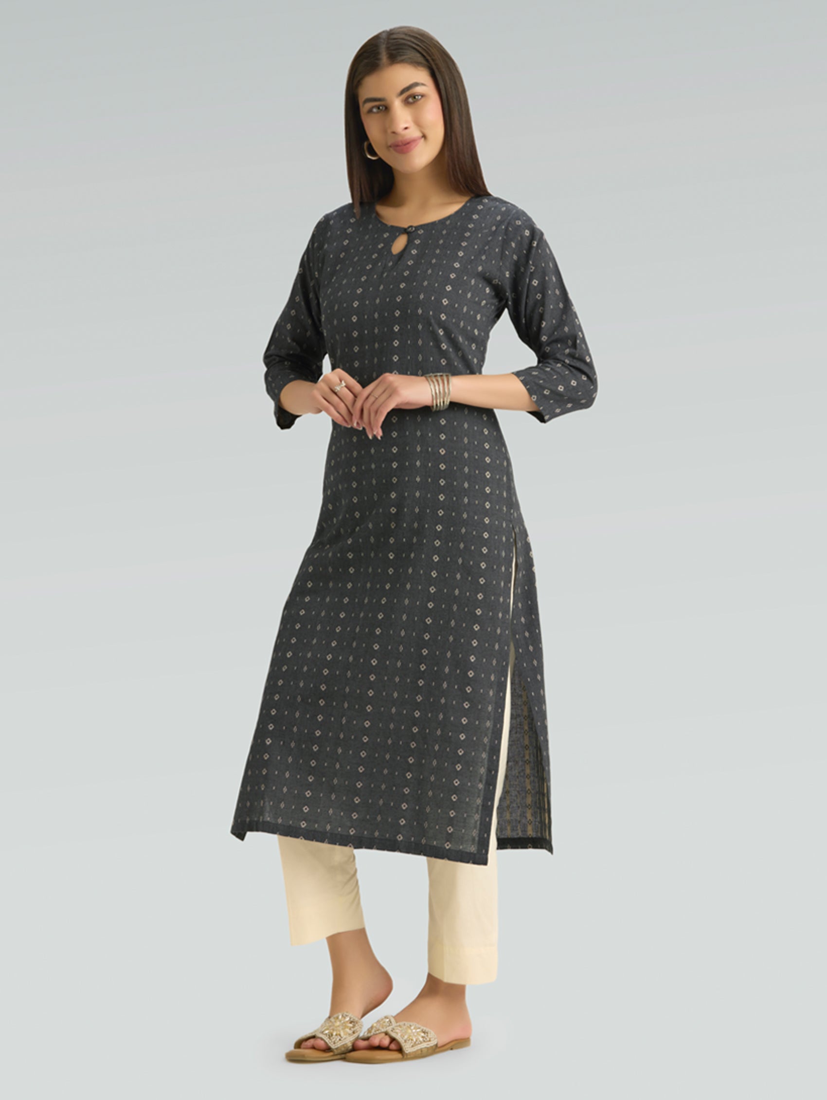 Woman wearing a dark gray patterned kurta with white pants on a light gray background