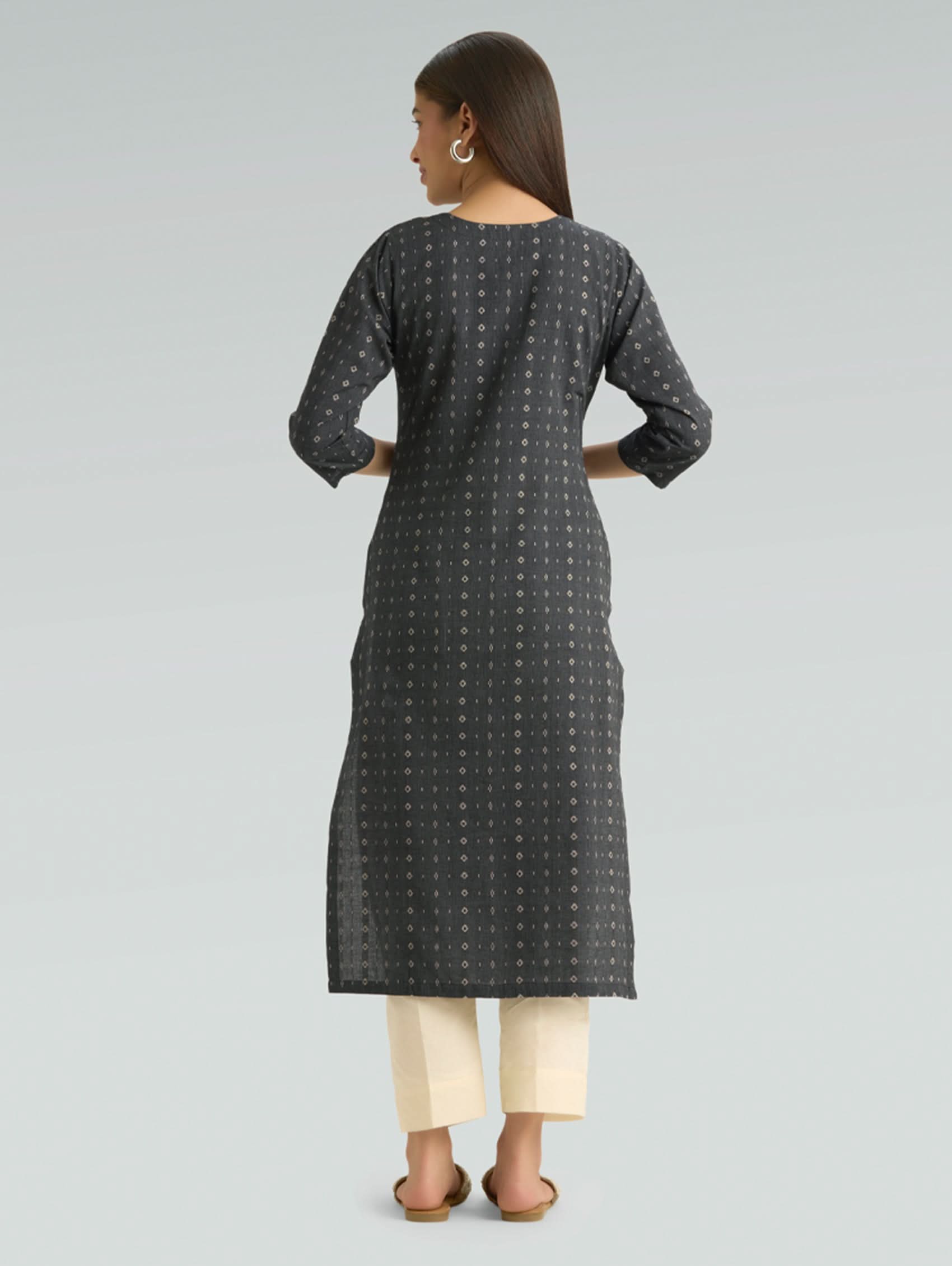 Woman wearing a black patterned kurta with white pants on a gray background