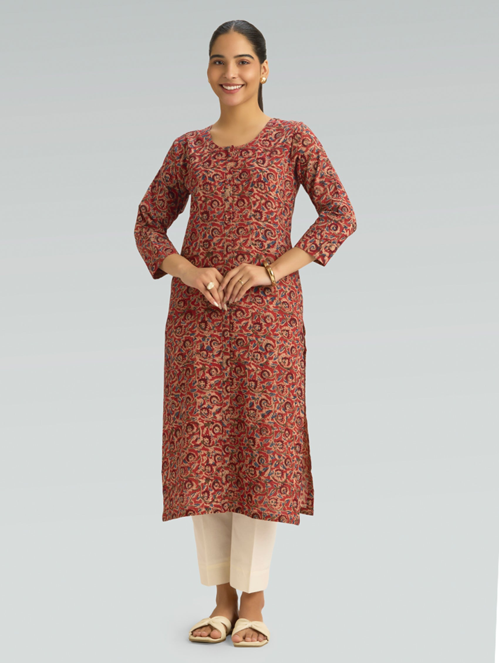 Woman wearing a red Kalamkari-patterned kurta with front and side slit white pants on a grey background