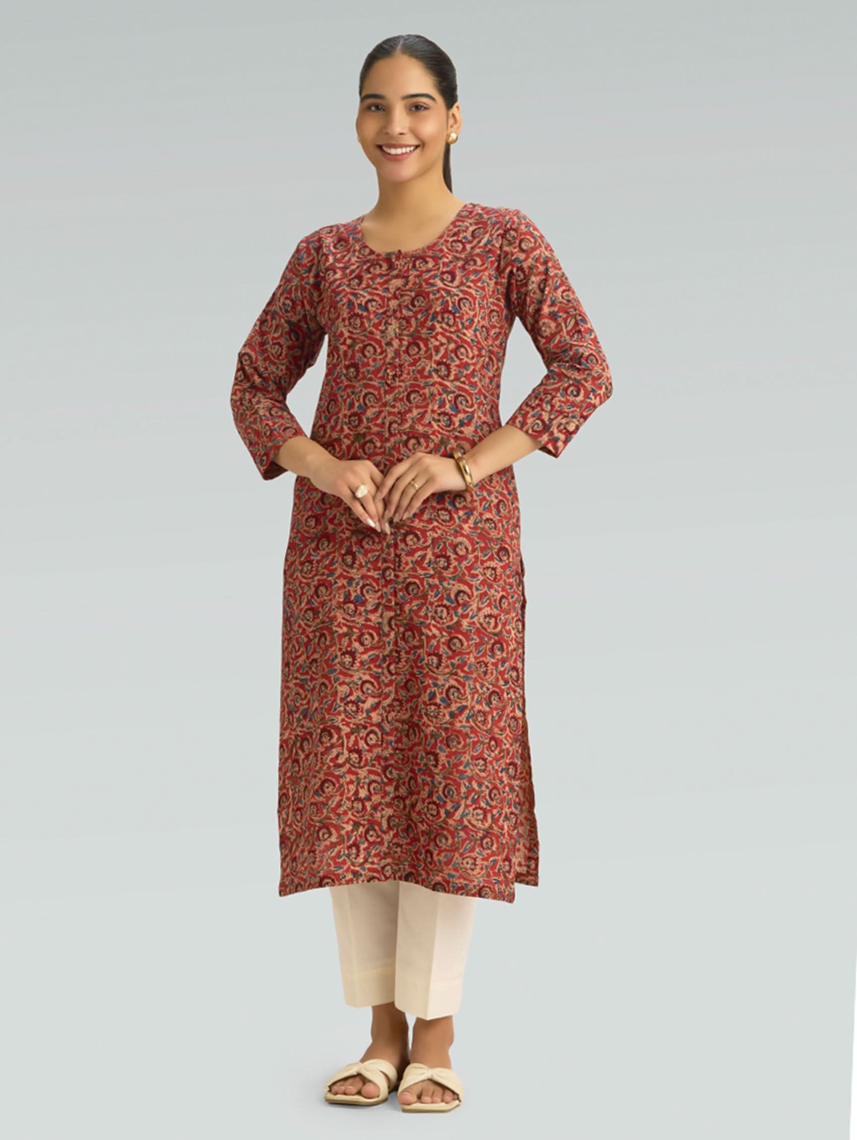 Woman wearing a red Kalamkari-patterned kurta with front and side slit white pants on a grey background