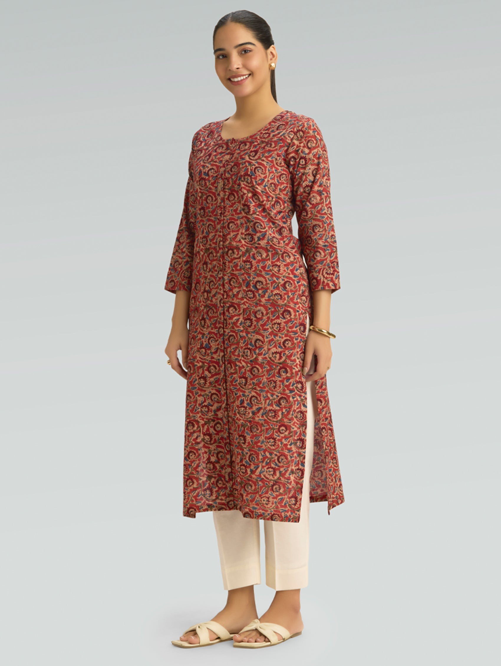 Woman wearing a red Kalamkari-patterned kurta with front and side slit white pants on a grey background