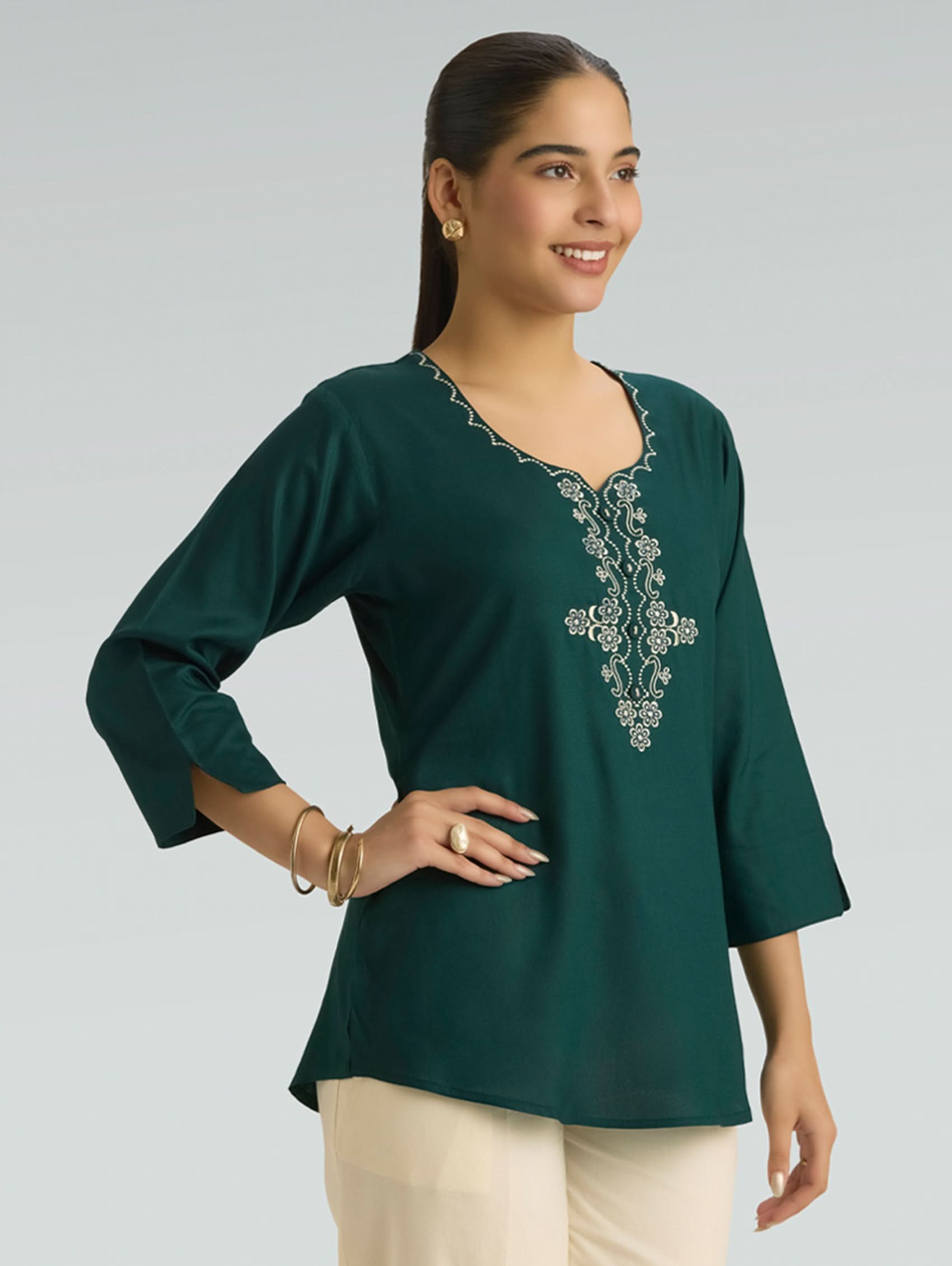 Woman wearing a green embroidered blouse against a gray background