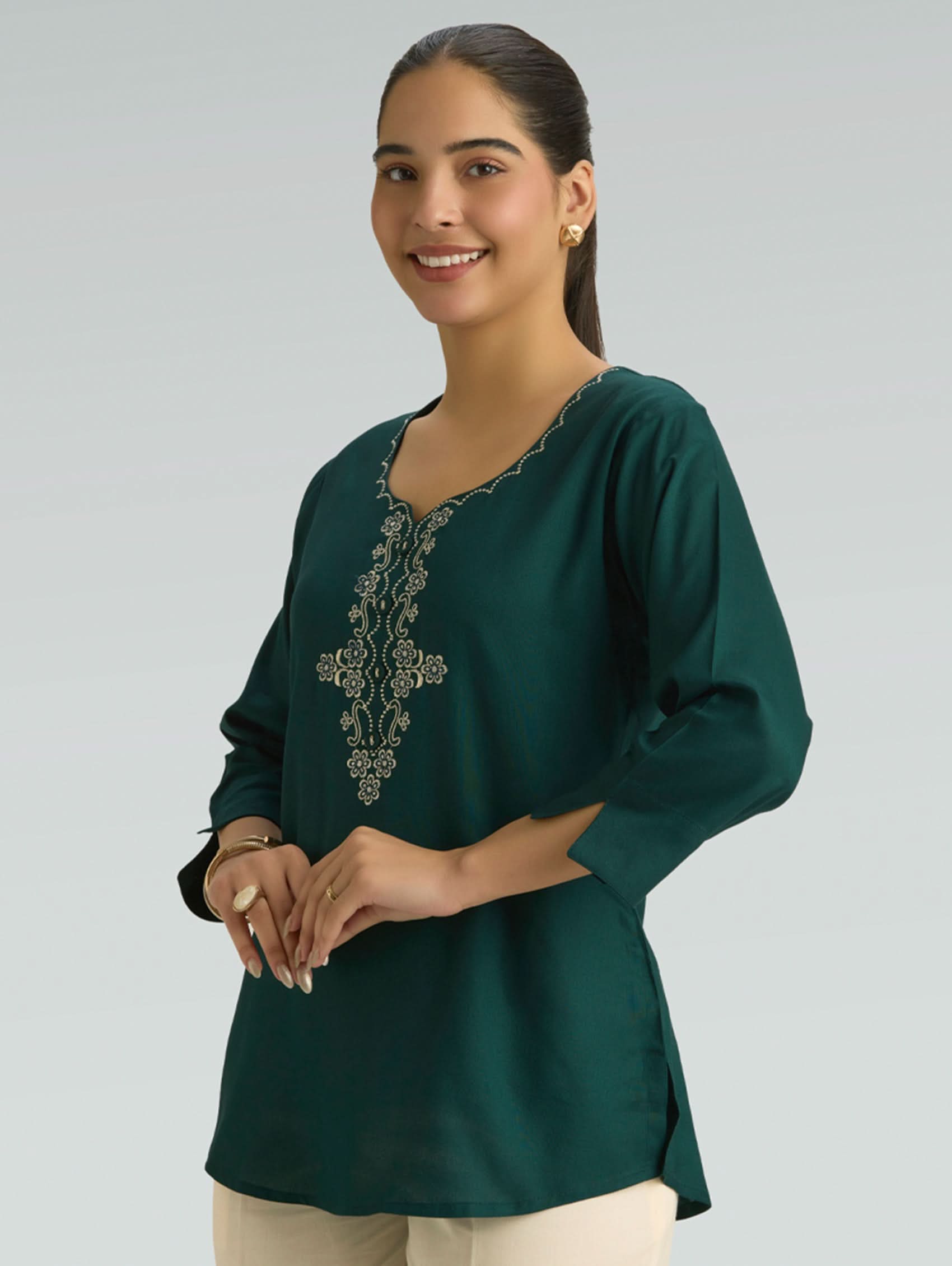 Woman wearing a green embroidered blouse against a plain background