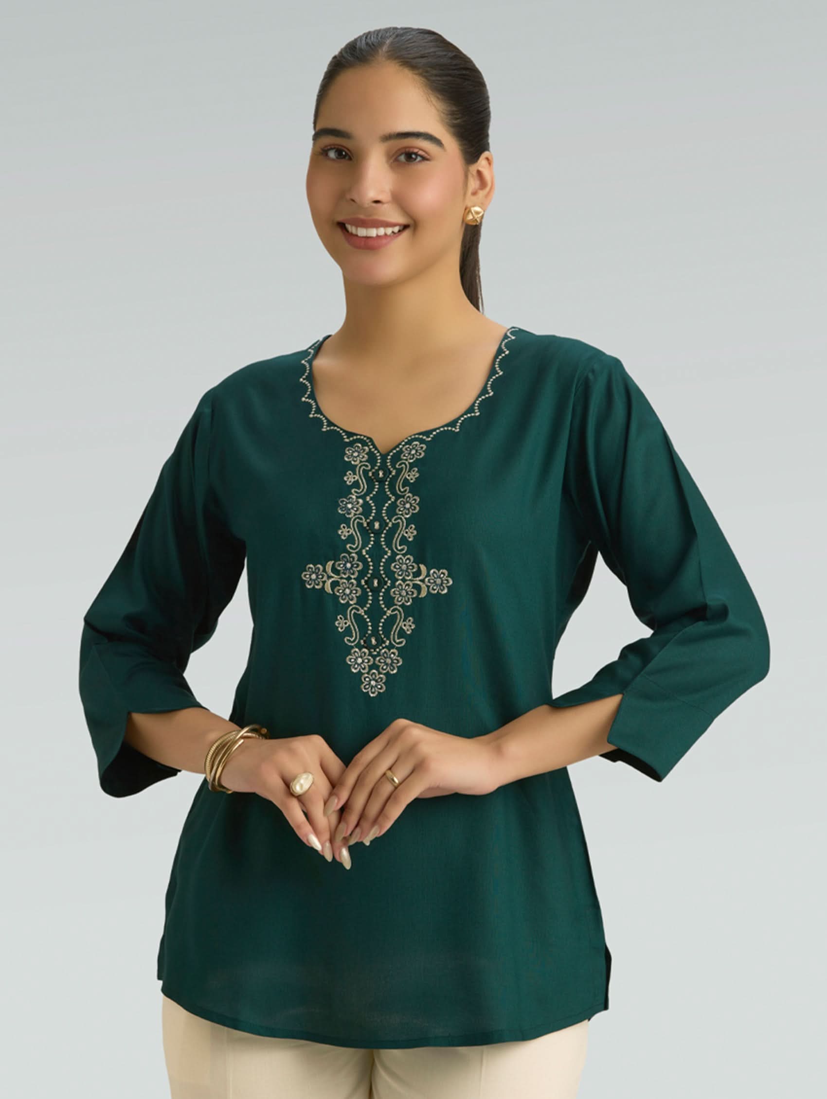 Woman wearing a green embroidered blouse against a gray background
