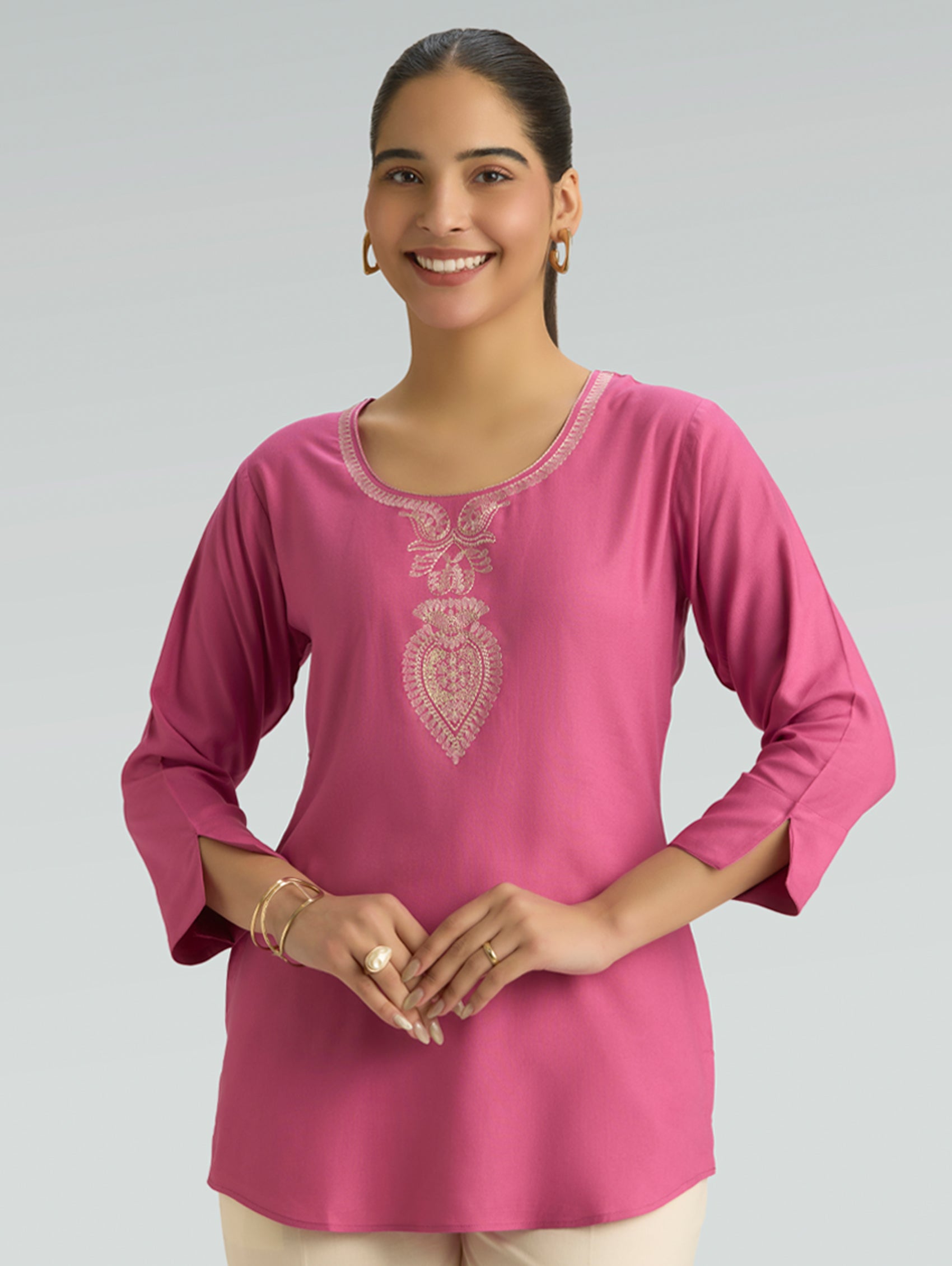 Woman wearing a pink embroidered top against a gray background