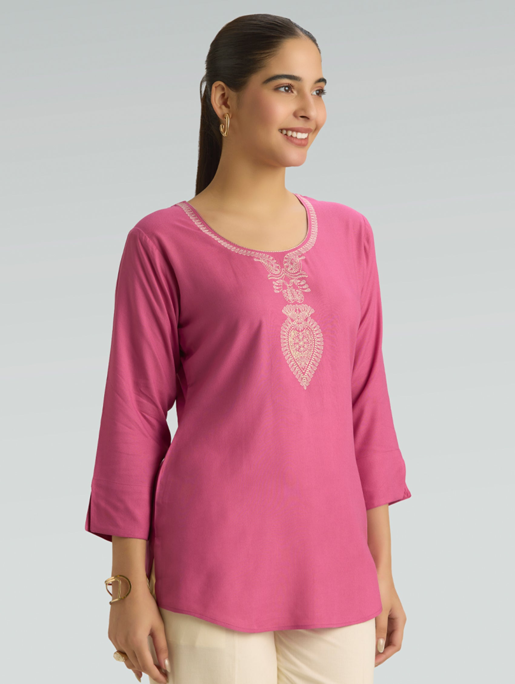 Woman wearing a pink embroidered top against a gray background