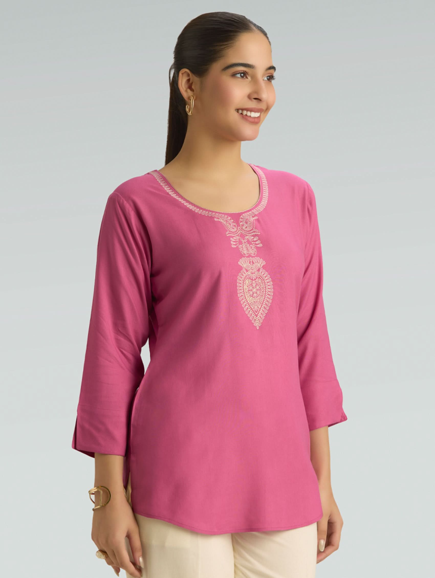Woman wearing a pink embroidered top against a gray background