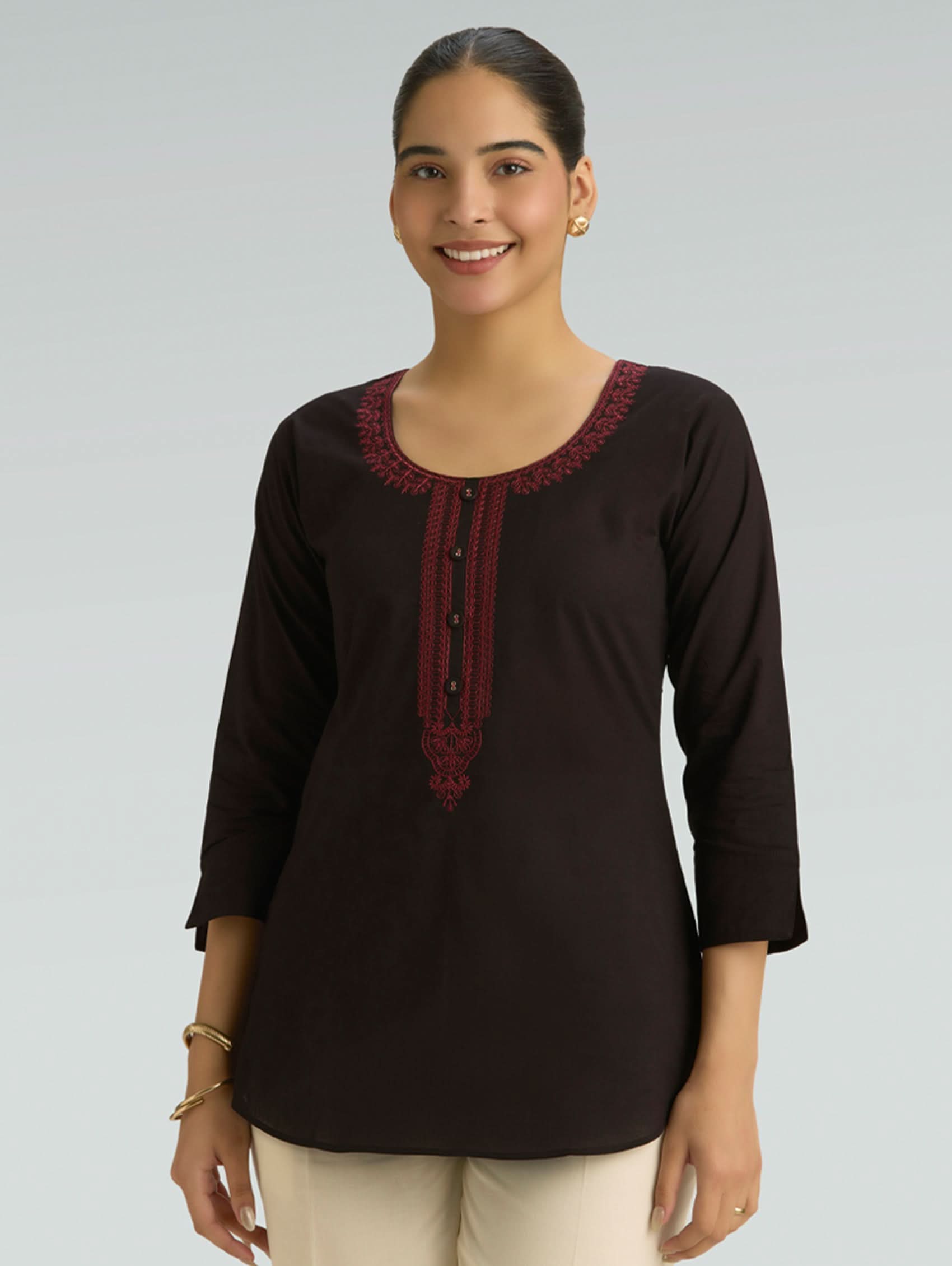 Woman wearing a black top with maroon embroidery on a gray background