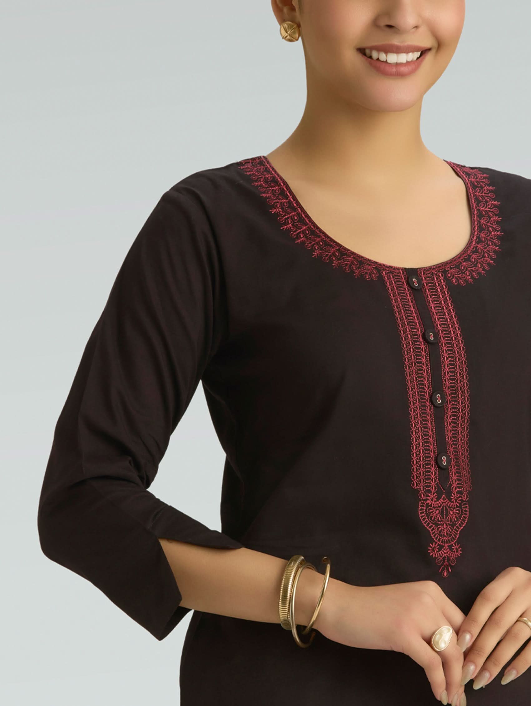 Woman wearing a black top with red embroidery on a gray background