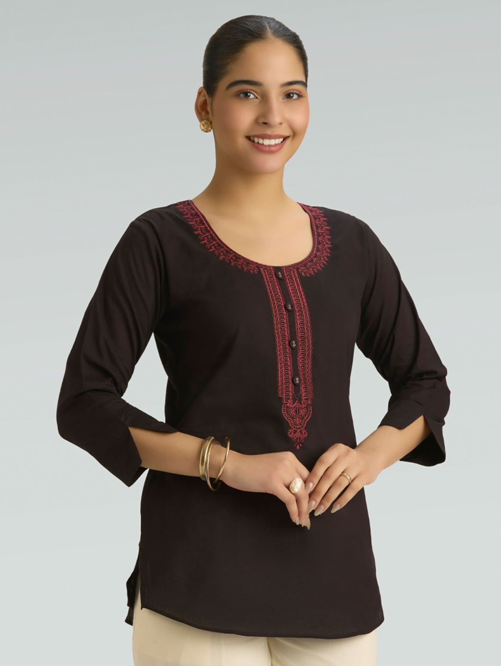 Woman wearing a black top with red embroidery on a gray background