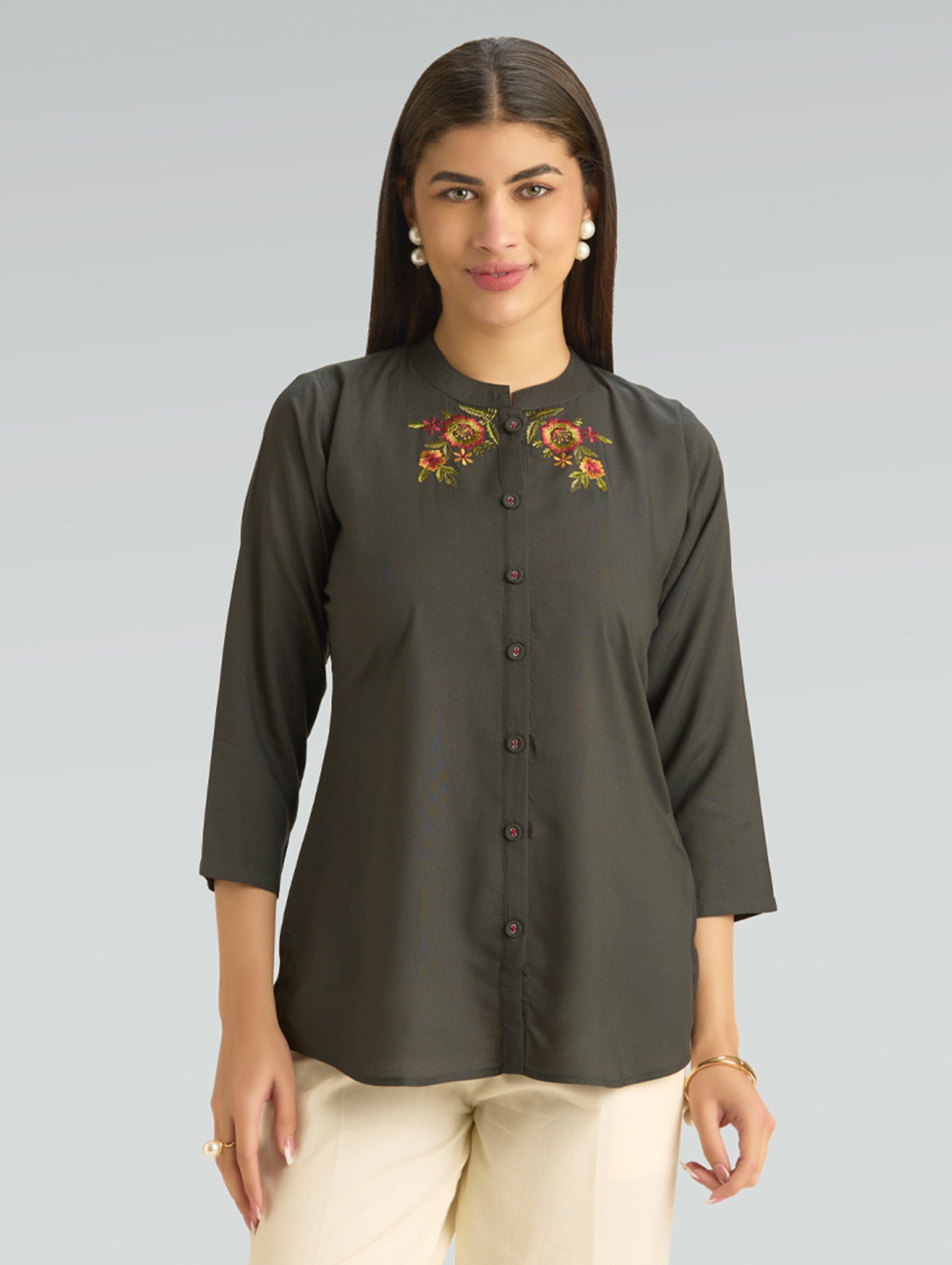 Woman wearing a dark green blouse with floral embroidery on a gray background