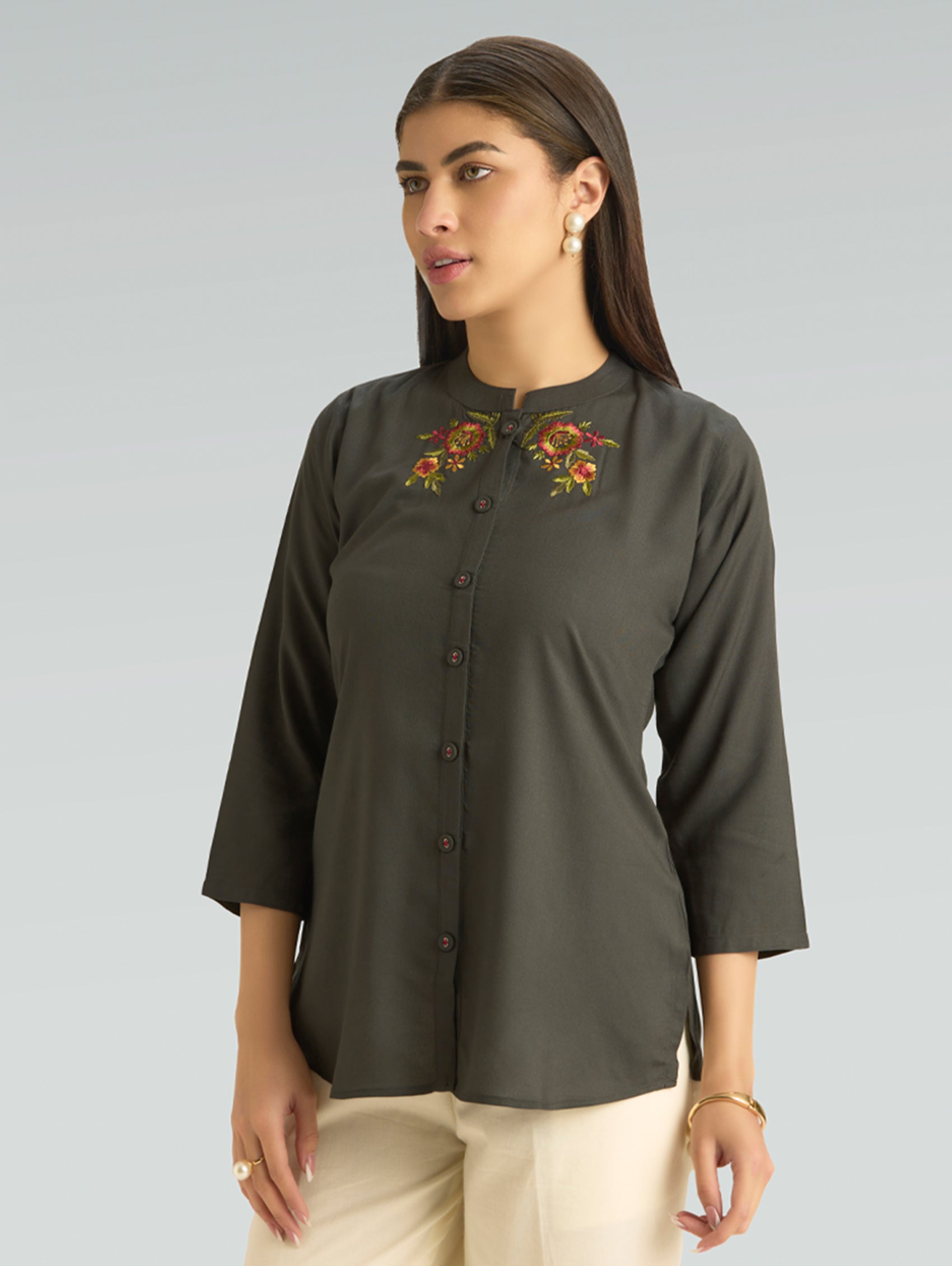 Woman wearing a dark green blouse with floral embroidery on a gray background