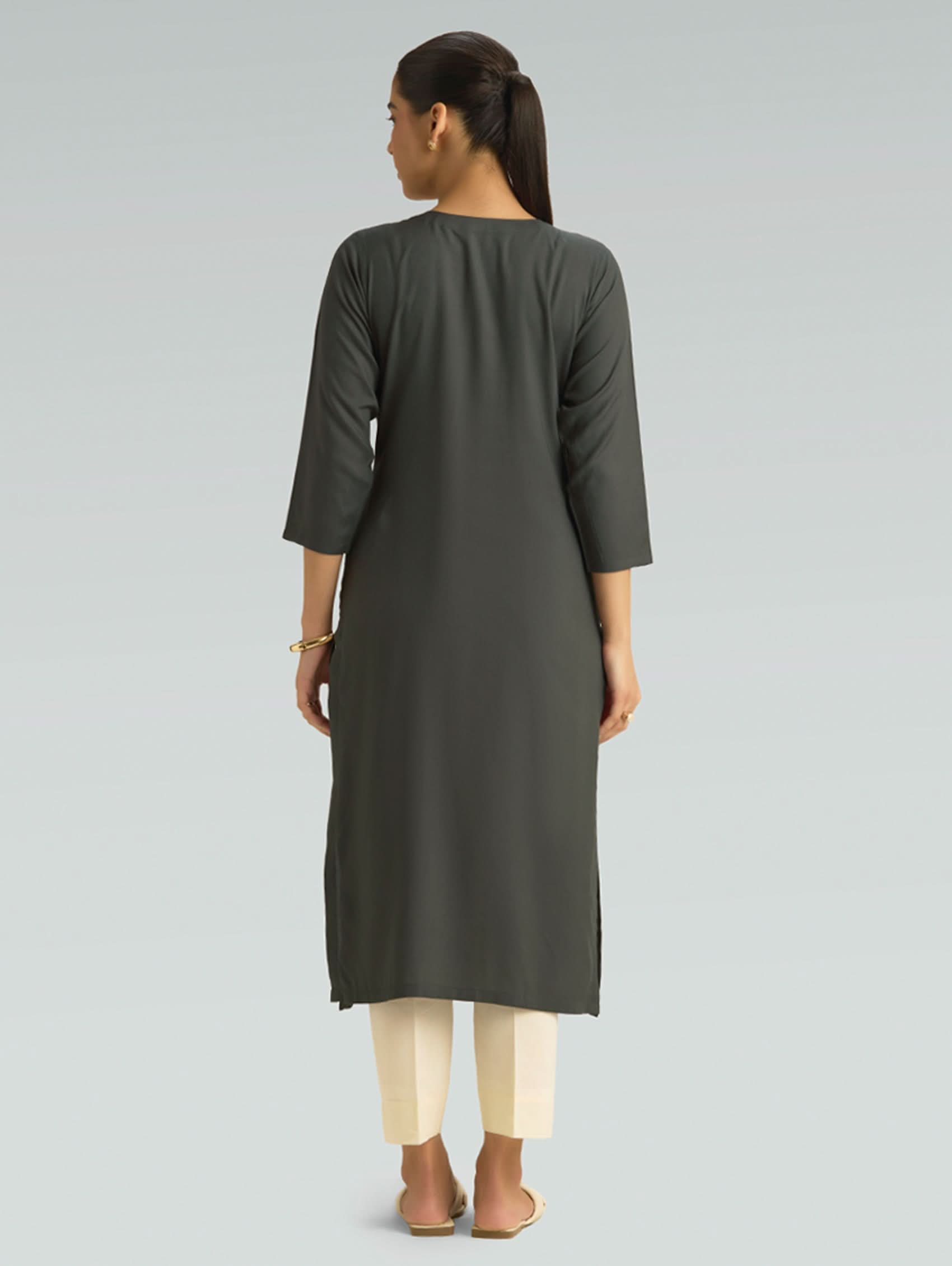 Woman wearing a dark gray kurta with white pants on a light gray background