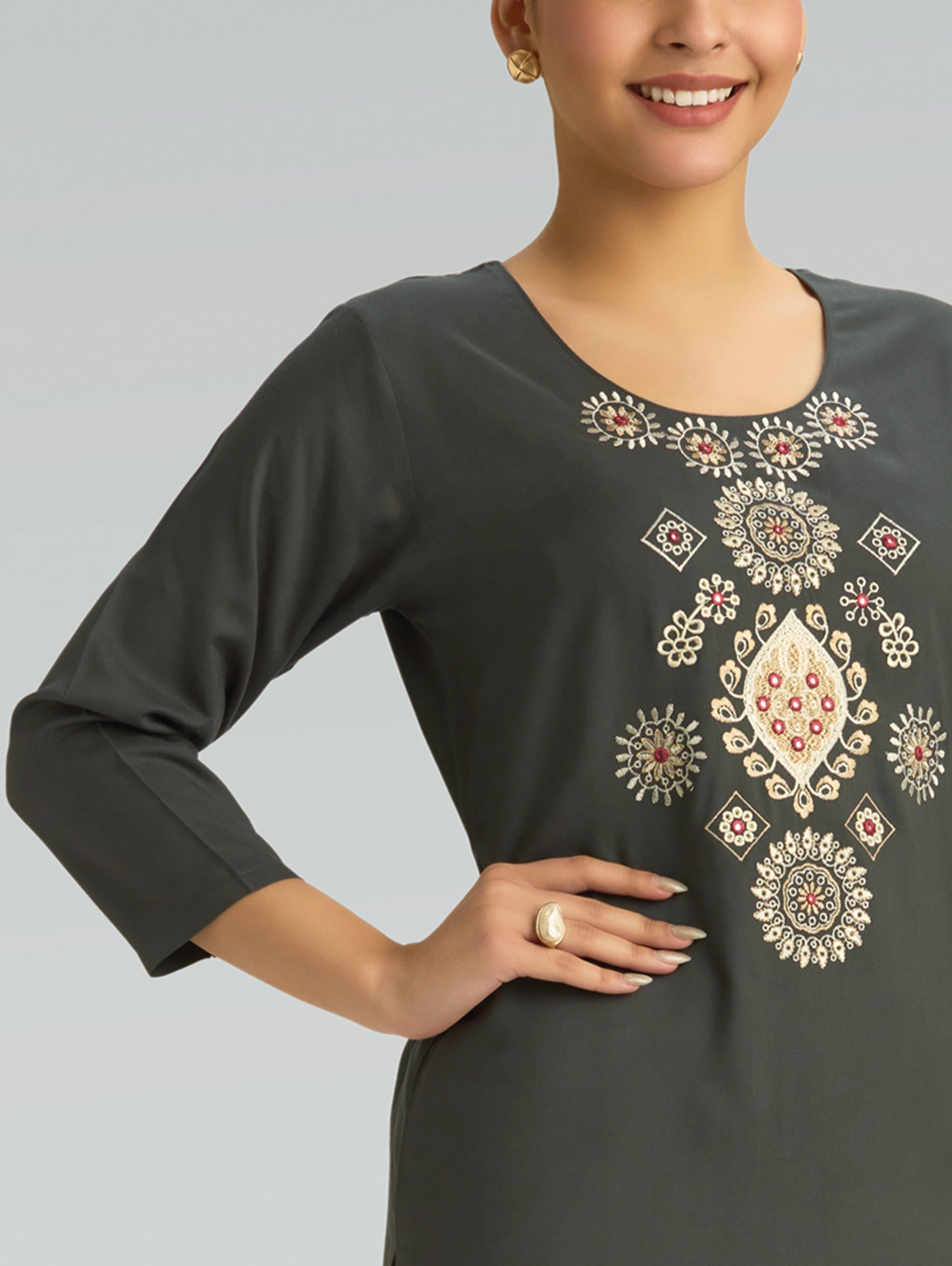 Woman wearing a dark gray dress with intricate white embroidery on a light gray background