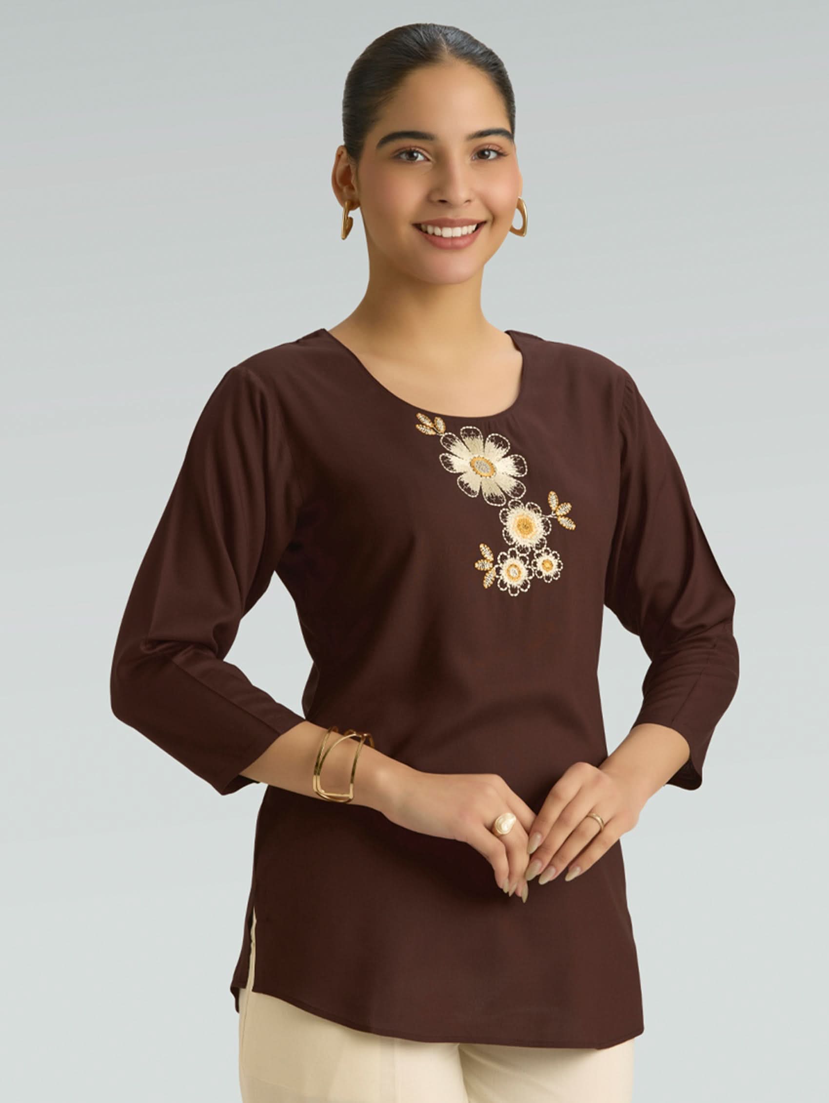 Woman wearing a brown long-sleeve top with floral embroidery on a plain background