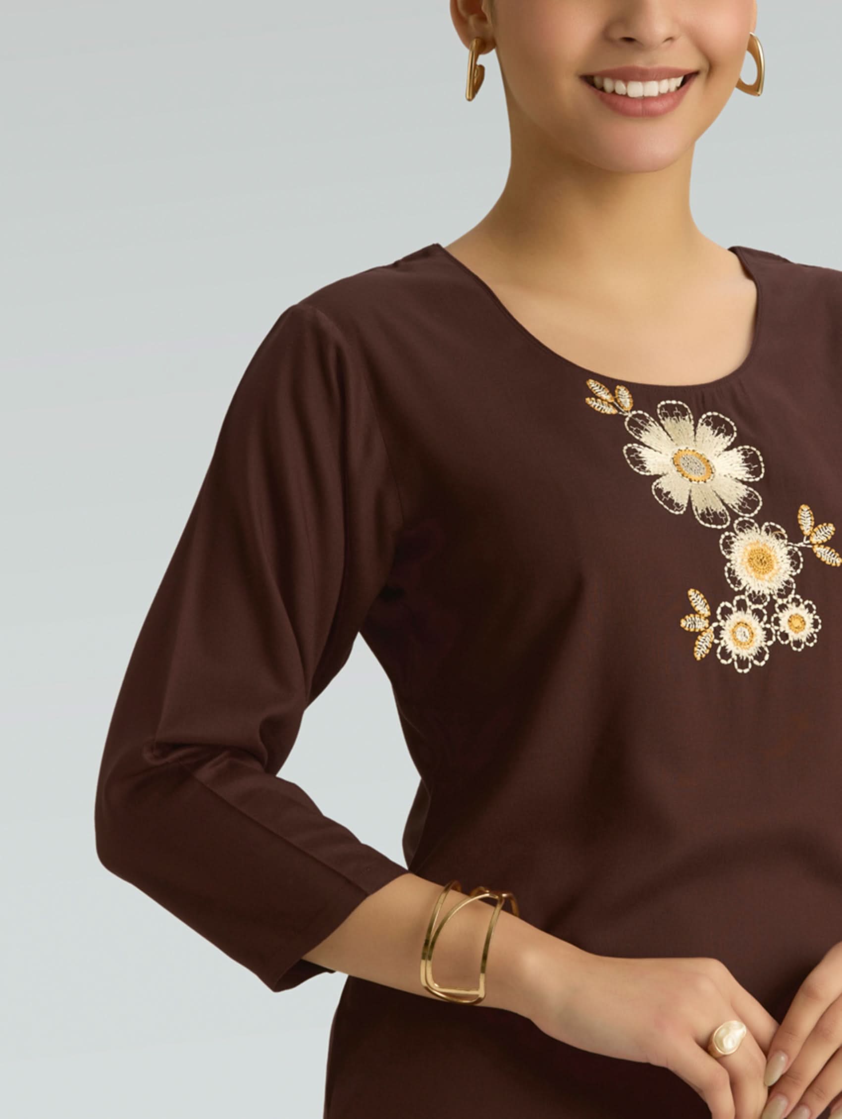 Woman wearing a brown long-sleeve top with floral embroidery on a plain background