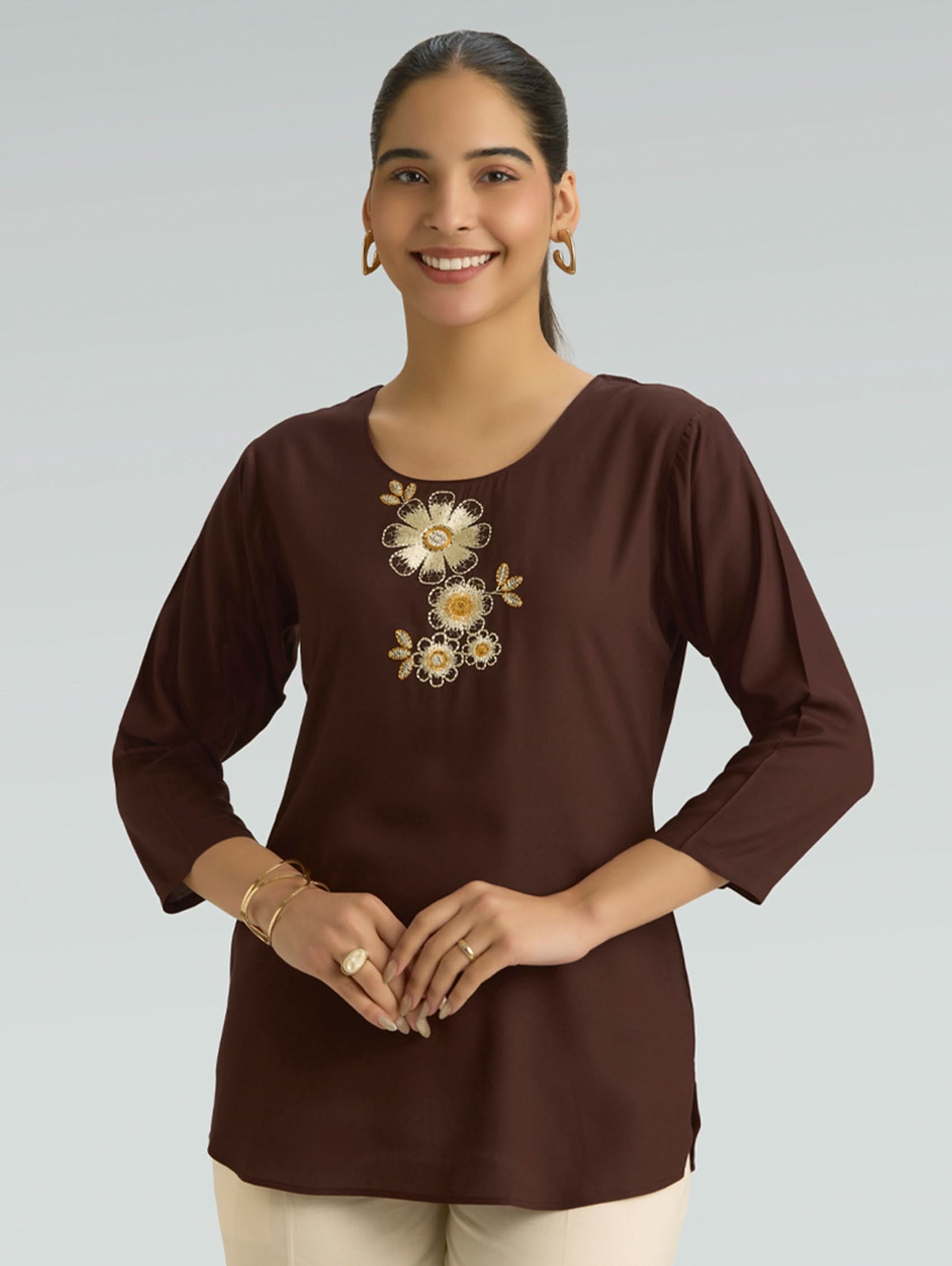 Woman wearing a brown blouse with floral embroidery on a plain background