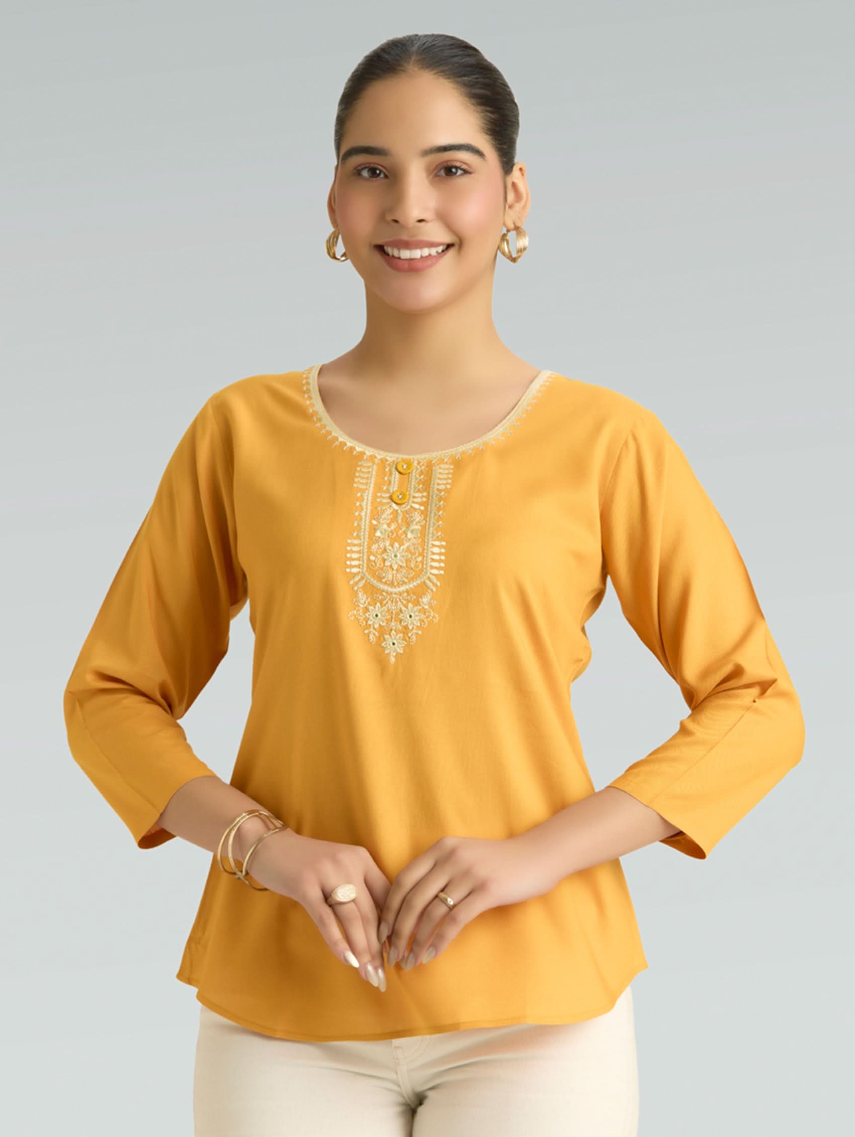 Woman wearing a mustard yellow top with intricate embroidery on a gray background