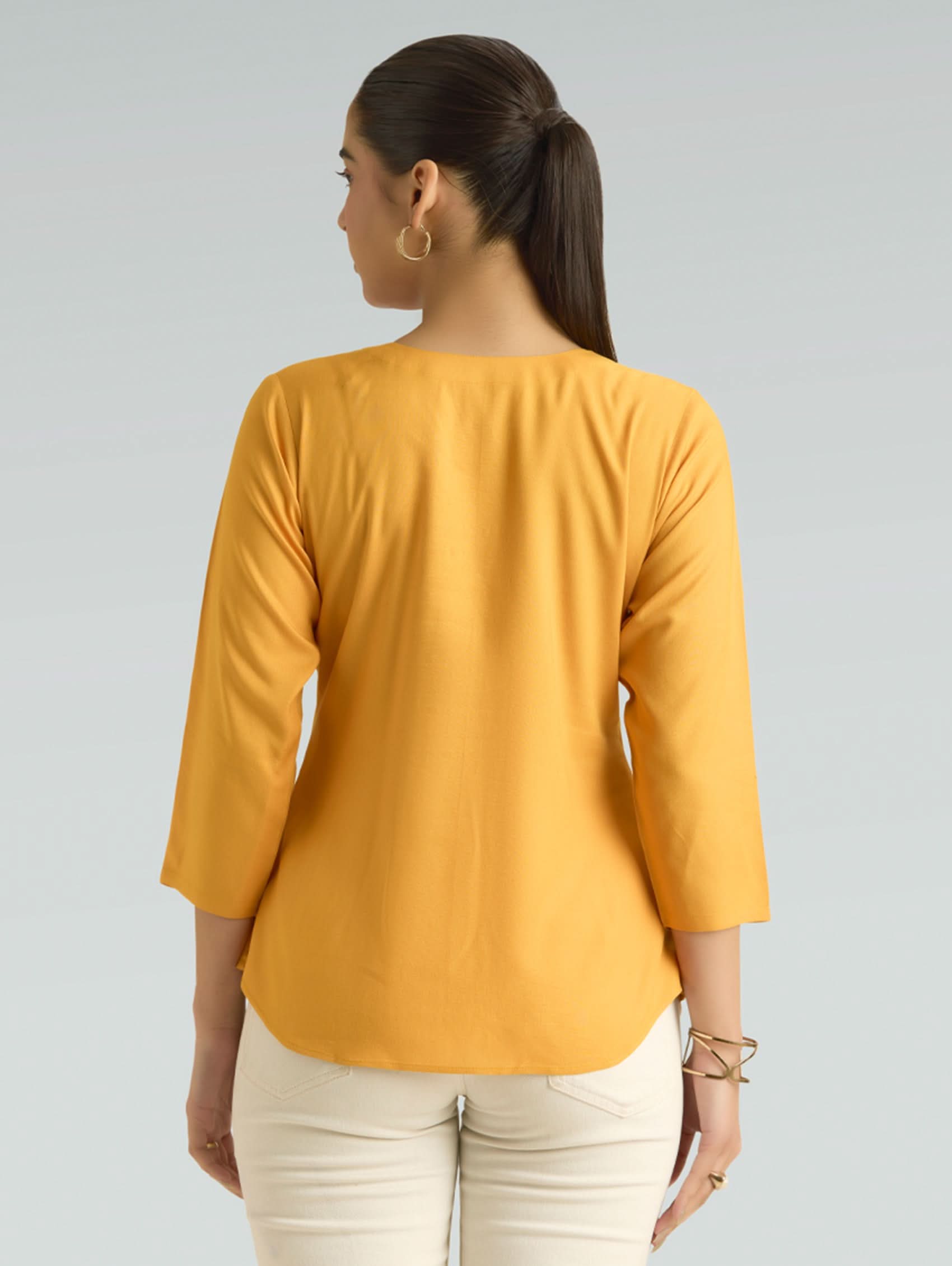 Woman wearing a mustard yellow top with three-quarter sleeves on a gray background