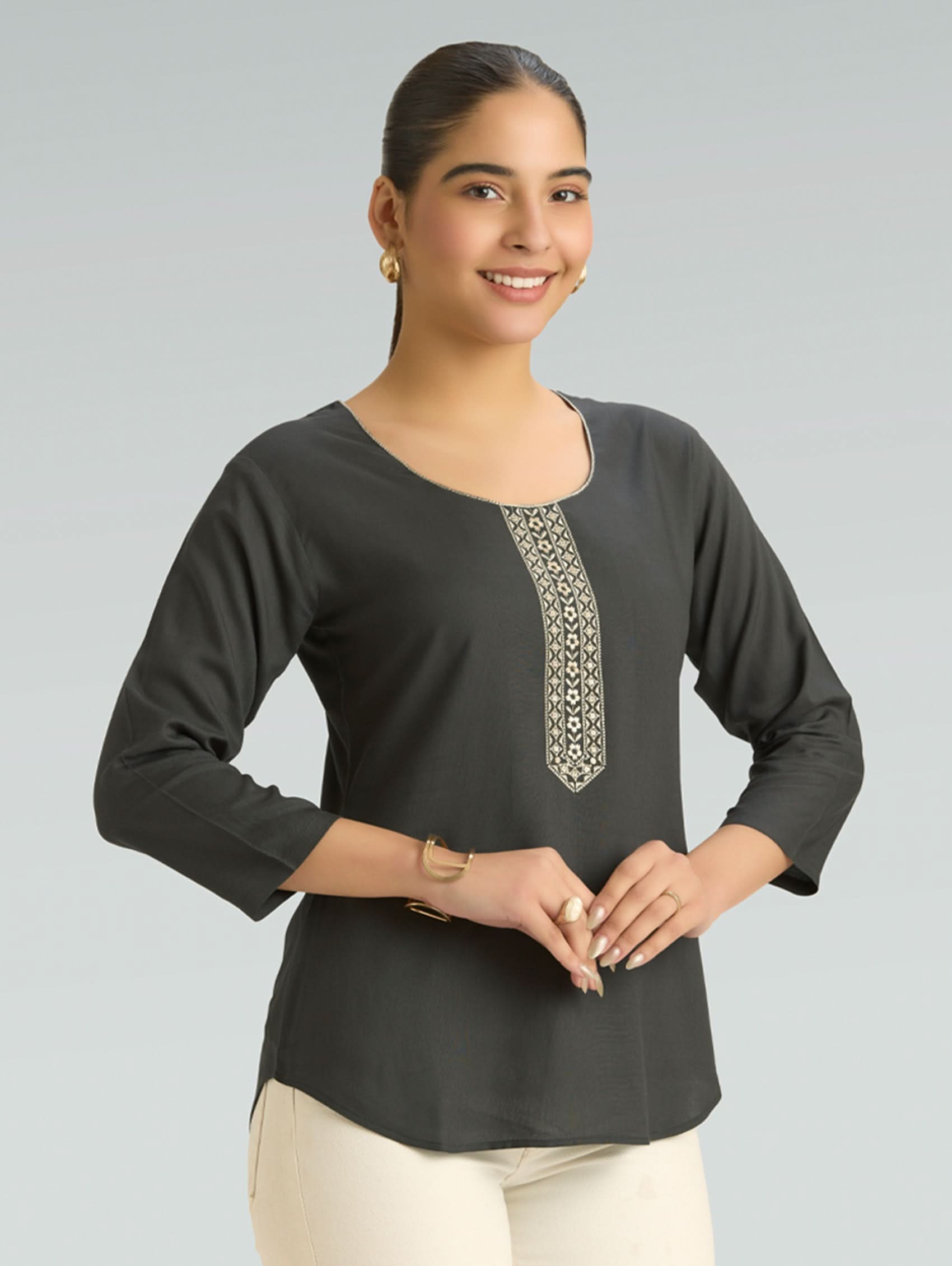Woman wearing a dark gray long-sleeve top with decorative embroidery on a plain background