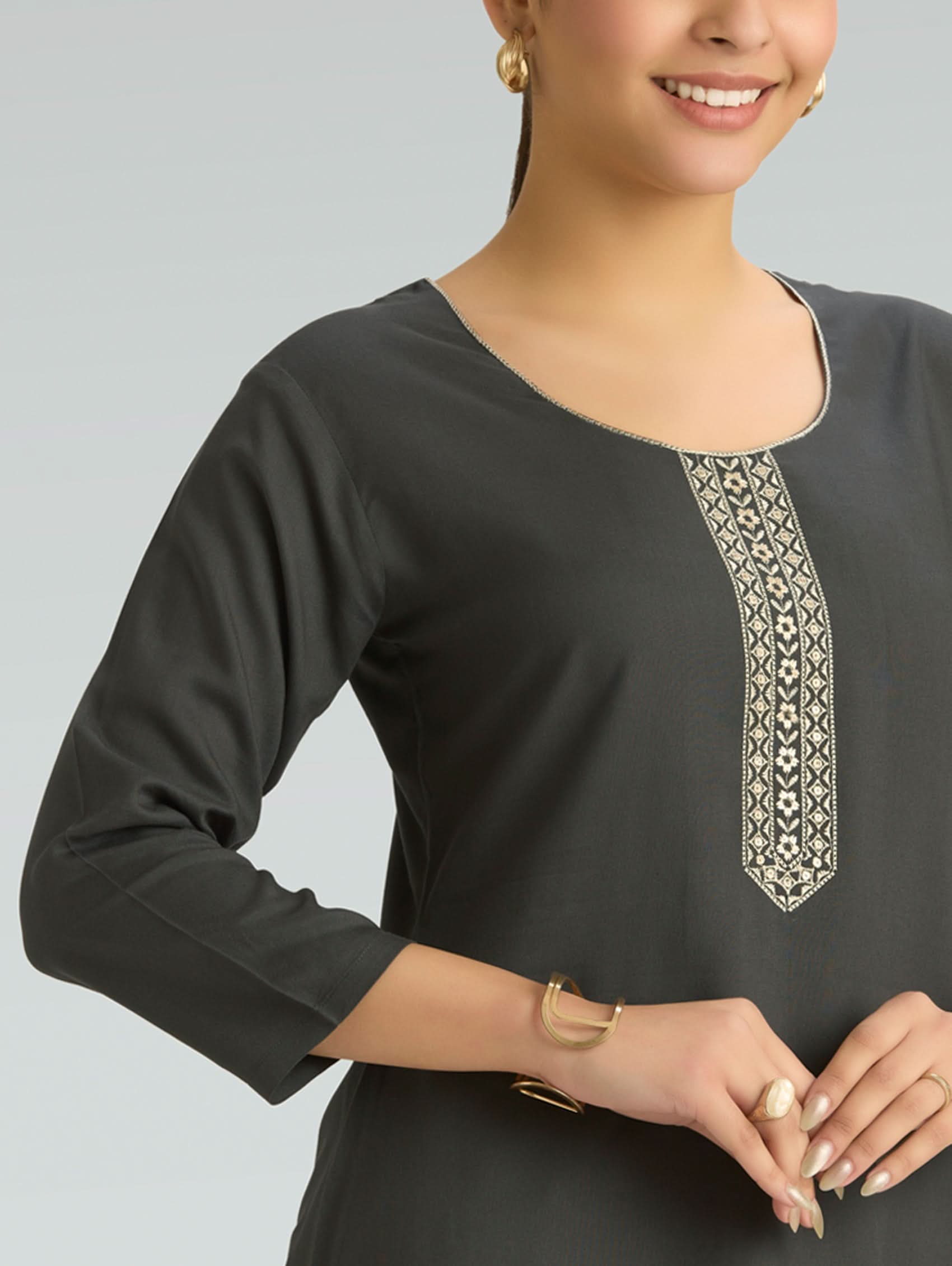 Woman wearing a dark gray long-sleeve top with decorative embroidery on a light gray background