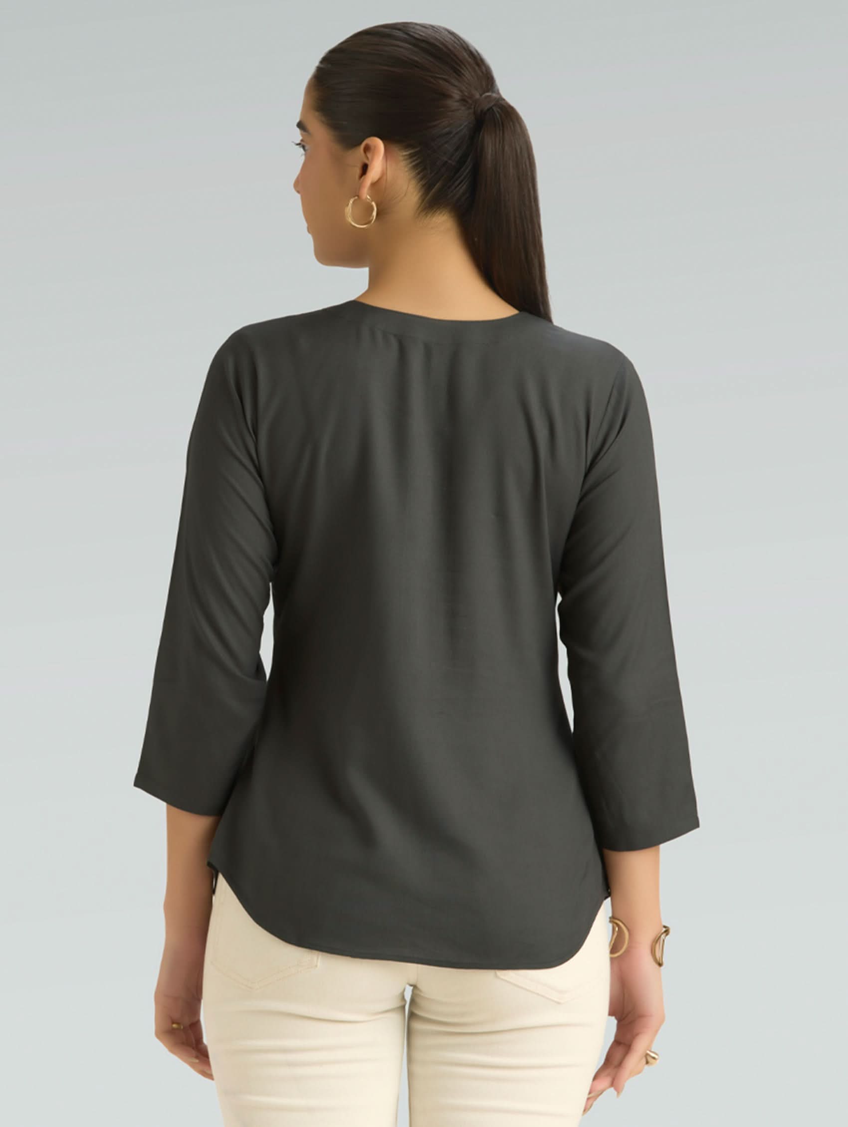 Woman wearing a dark gray top with 3/4 sleeves on a light gray background