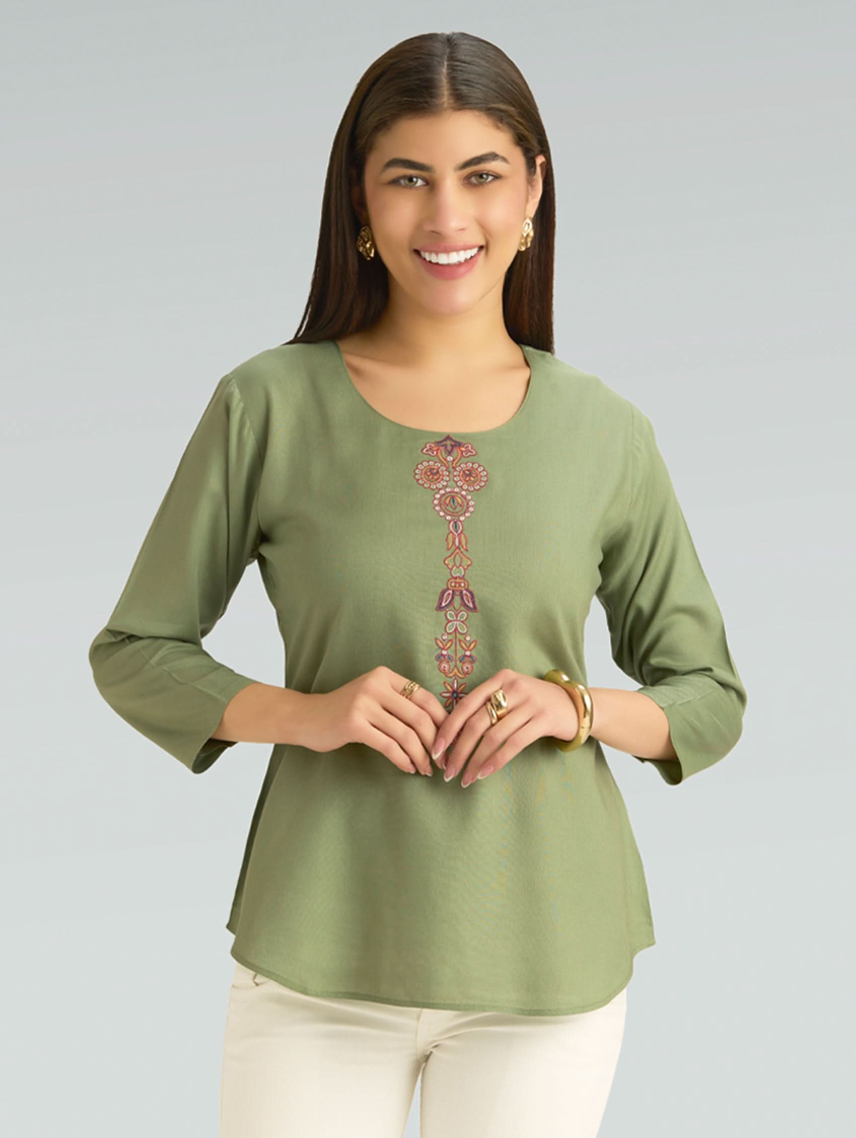 Woman wearing a green top with a decorative pattern on a gray background