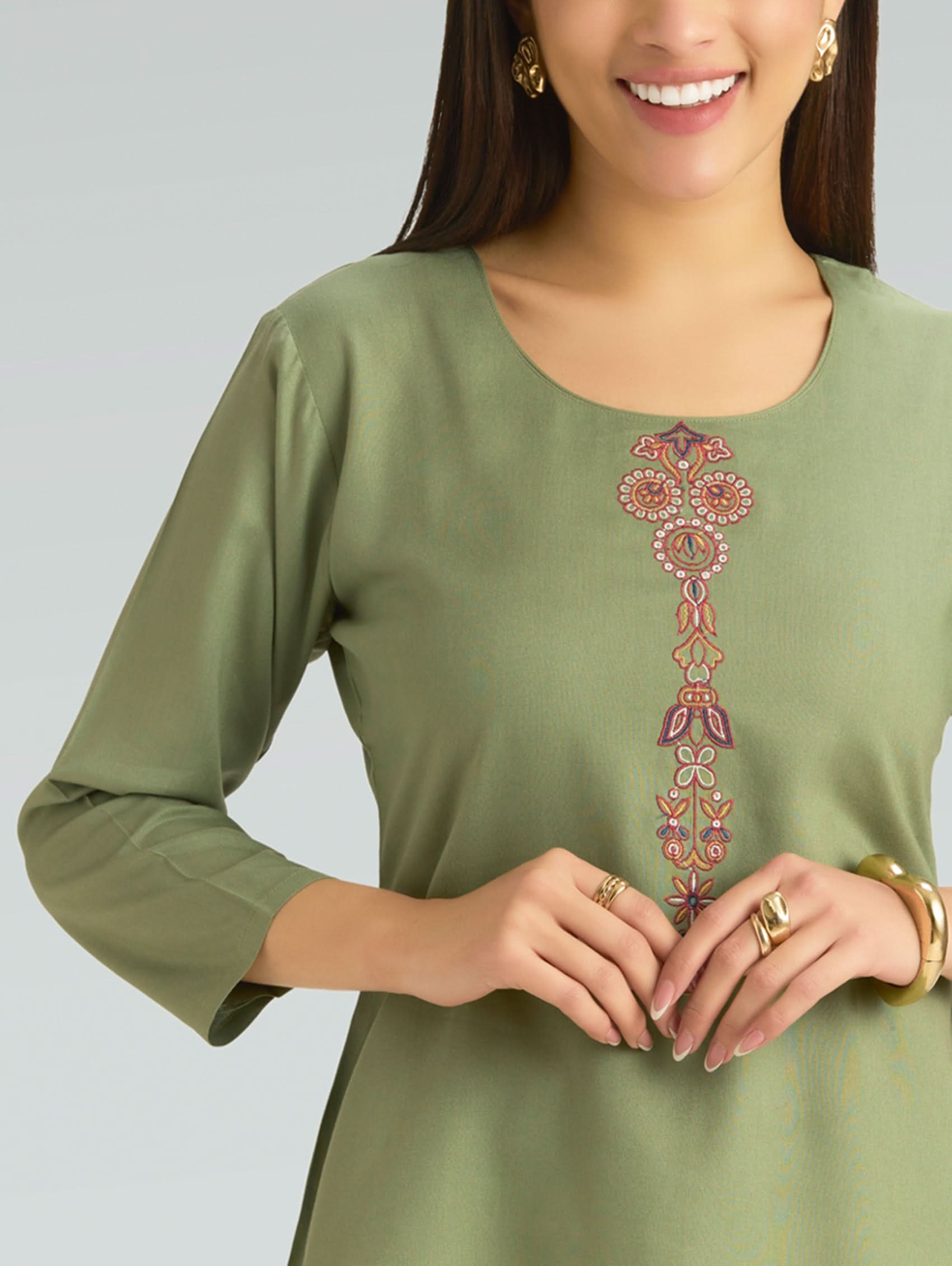 Woman wearing a green dress with floral embroidery on a plain background