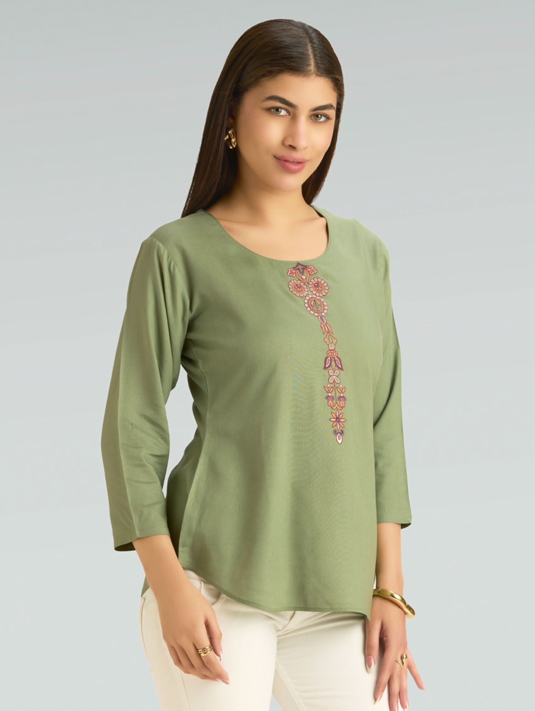 Woman wearing a green top with floral embroidery on a gray background