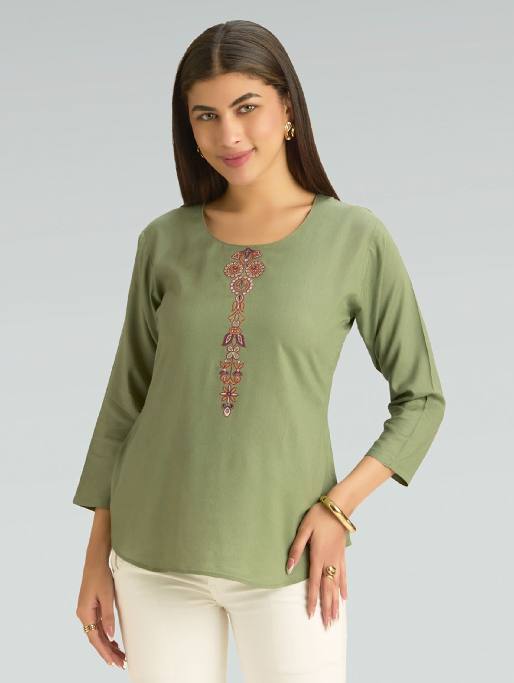 Woman wearing a green top with a decorative pattern on a gray background