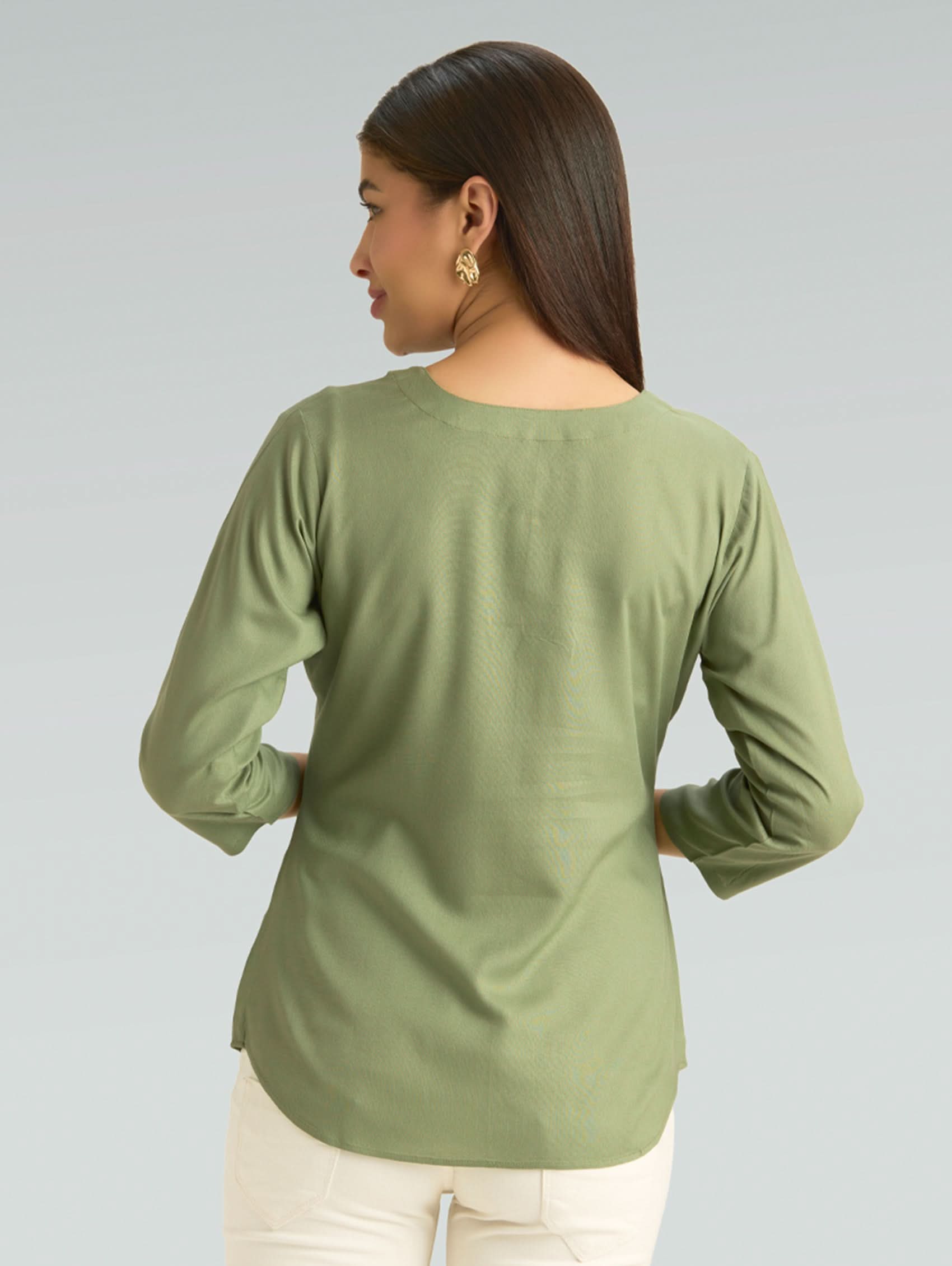 Woman wearing a green long-sleeve top on a gray background