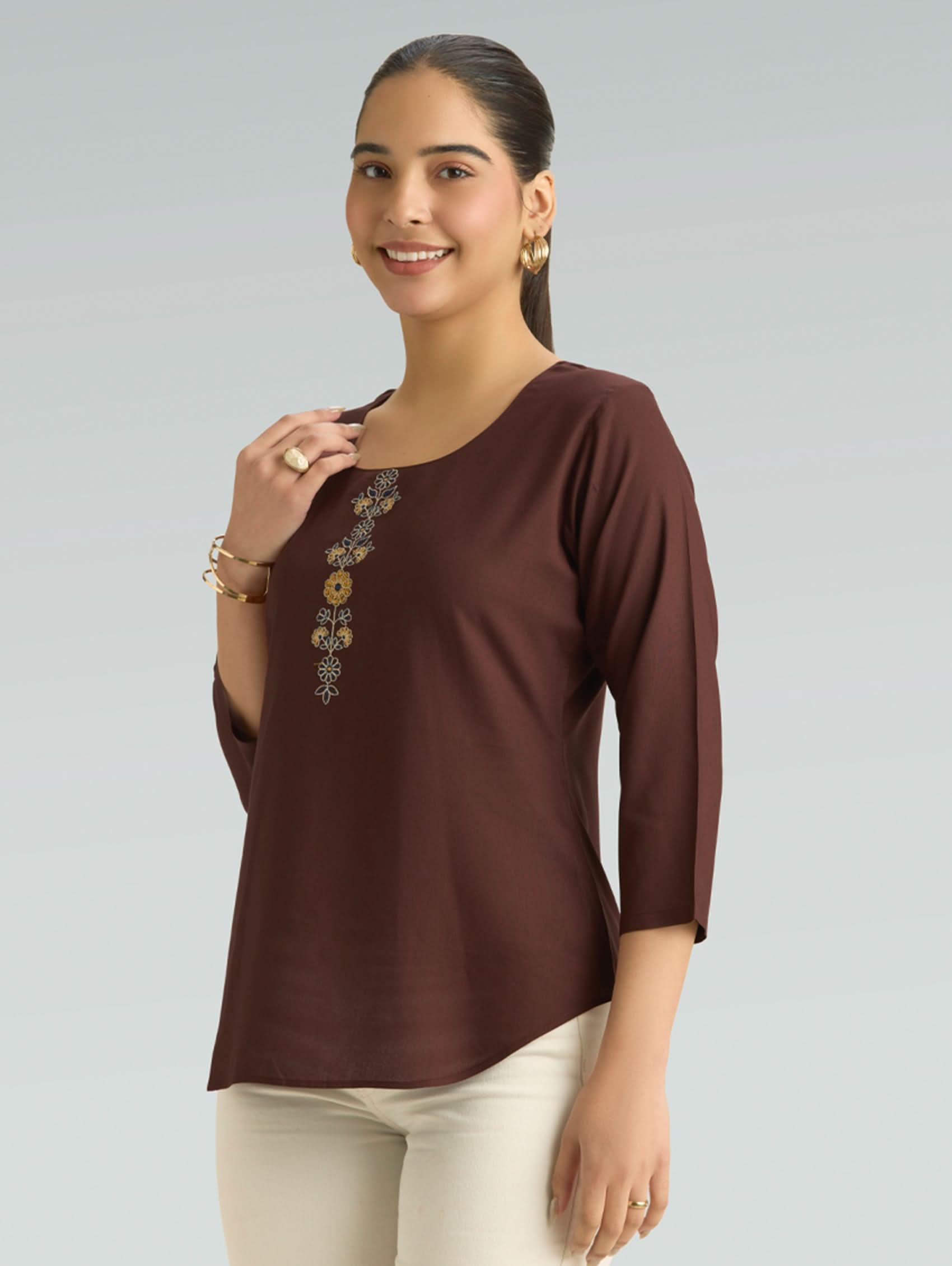 Woman wearing a brown top with floral embellishments on a gray background