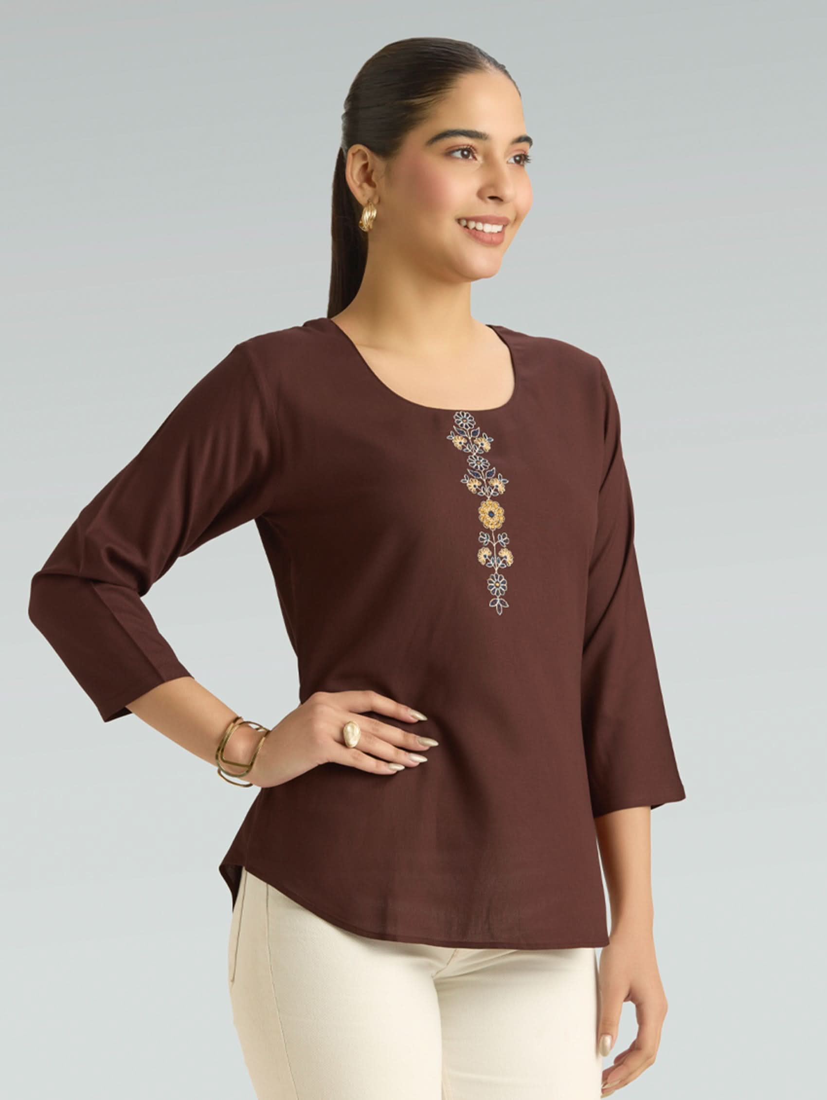 Woman wearing a brown blouse with floral embroidery on a gray background