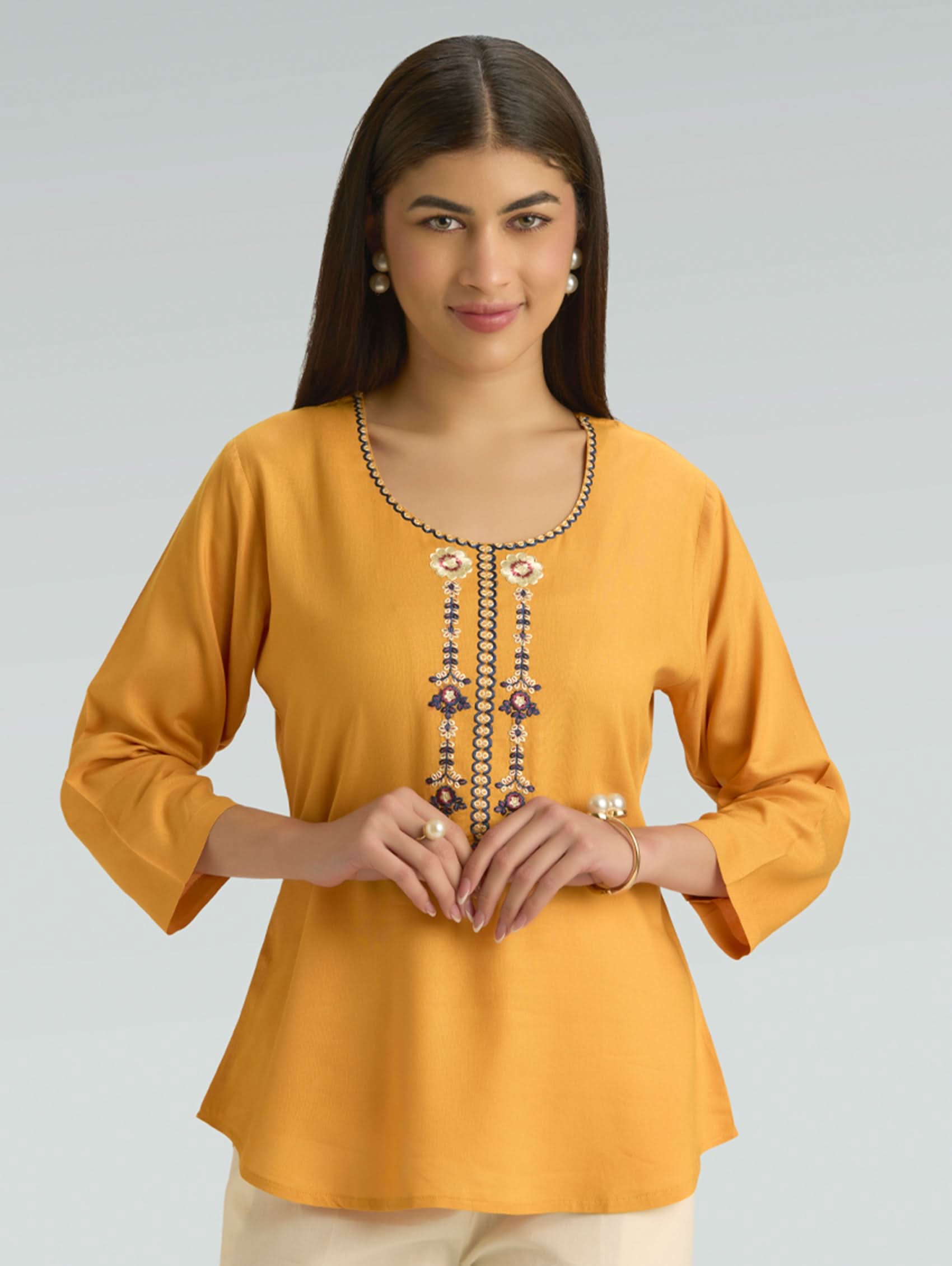 Woman wearing a mustard yellow top with intricate detailing on a gray background