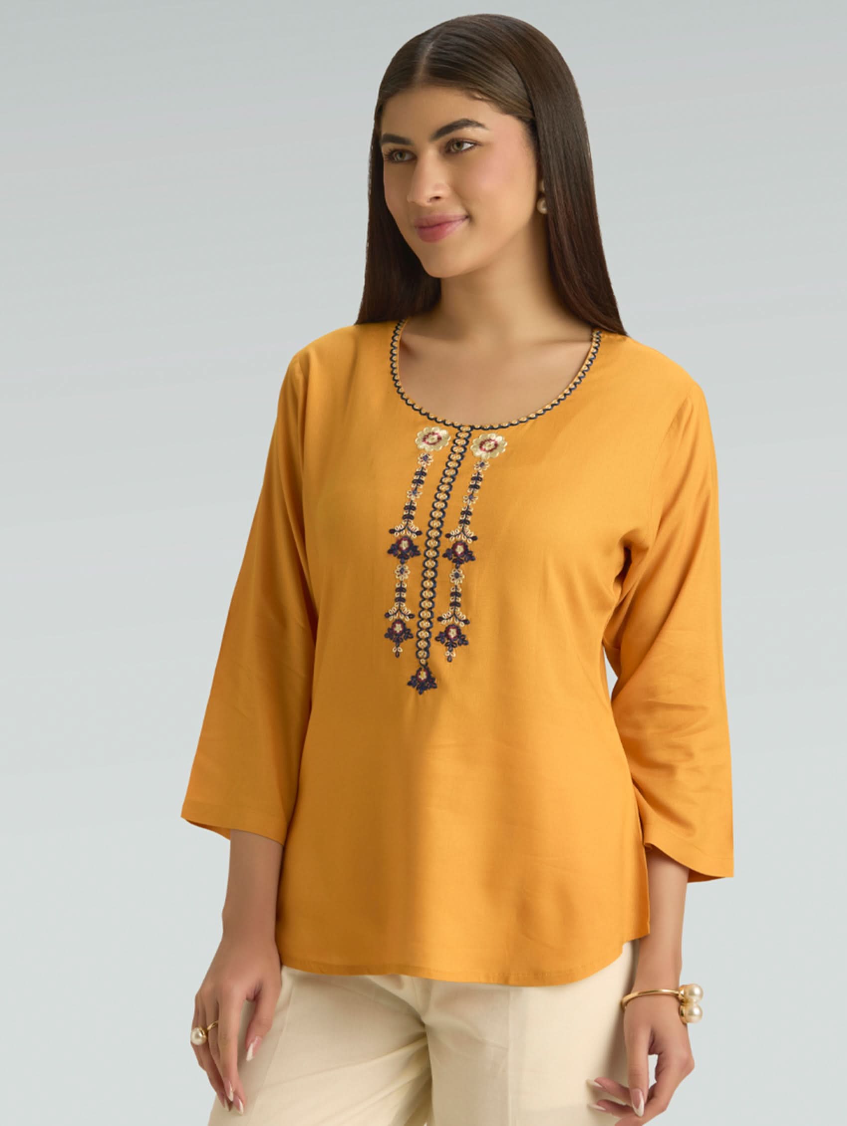 Woman wearing a mustard yellow top with intricate beadwork on a gray background