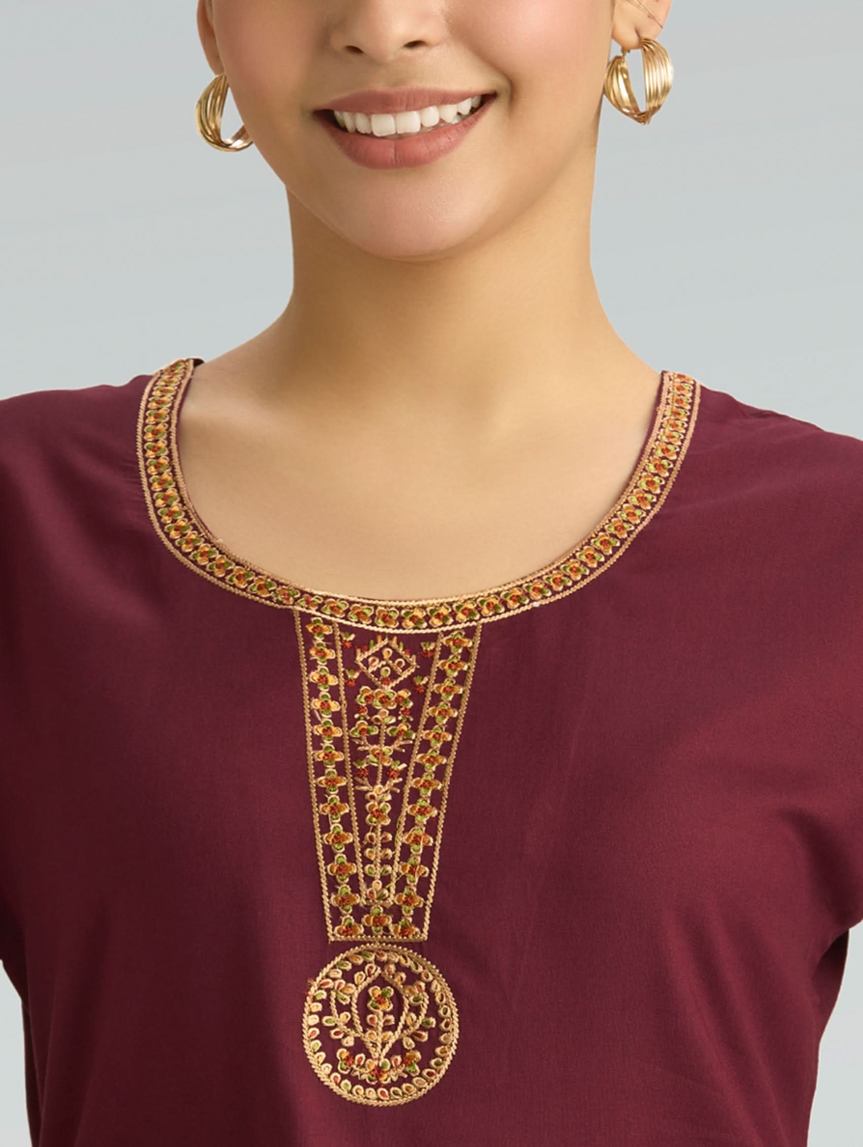 Close-up of a maroon top with gold embroidery on a plain background