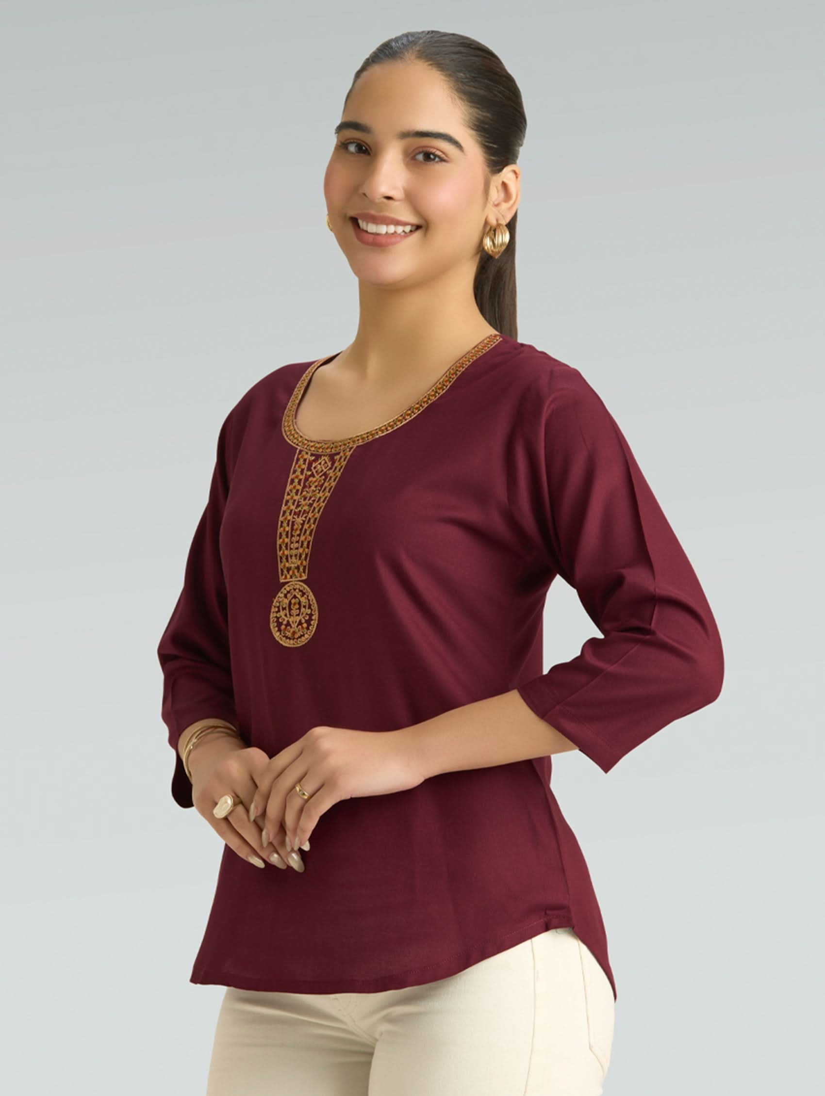 Woman wearing a burgundy top with gold embroidery on a gray background