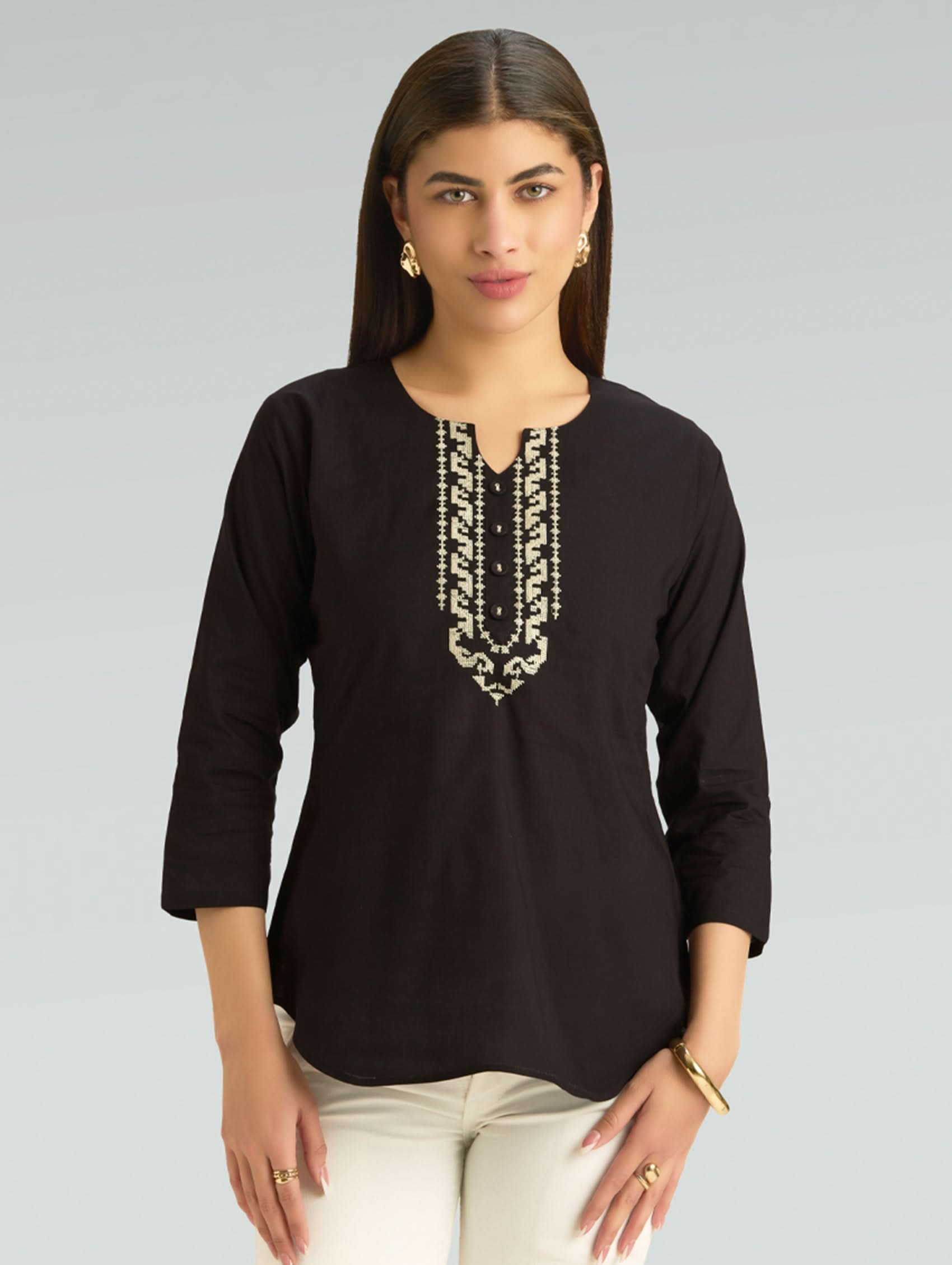 Woman wearing a black top with white embroidery on a gray background