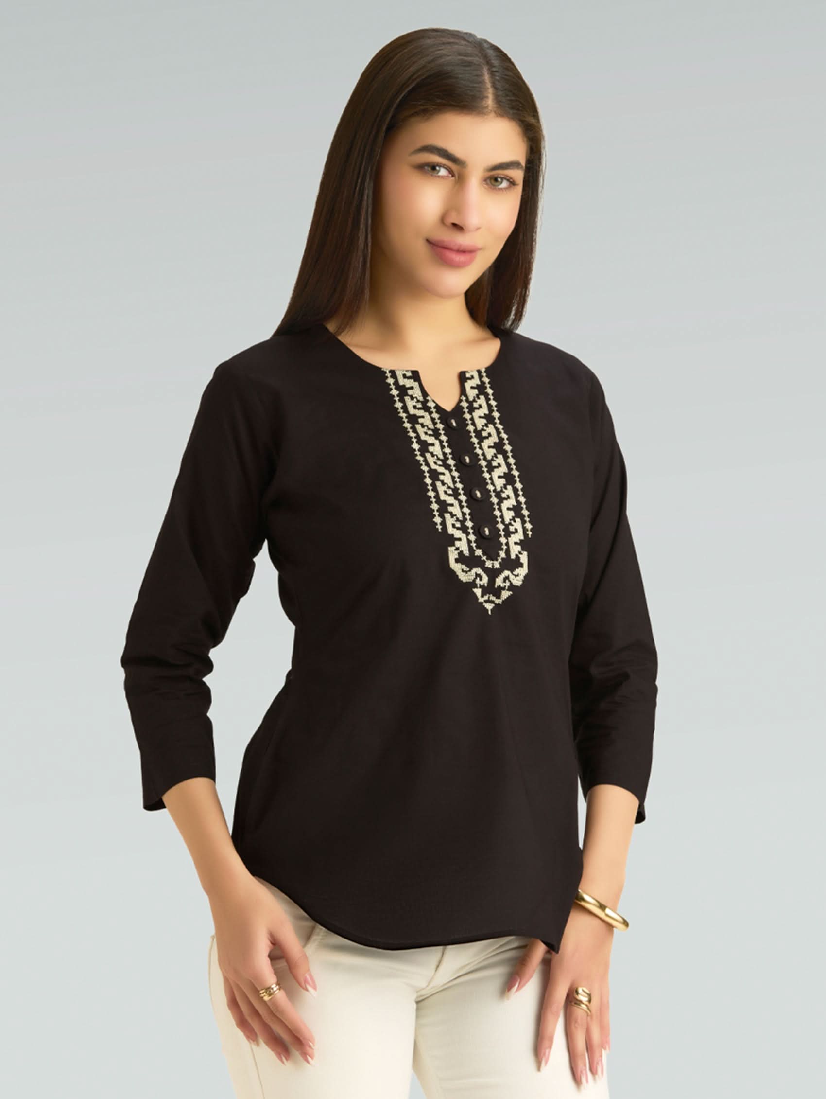 Woman wearing a black top with intricate white embroidery on a gray background