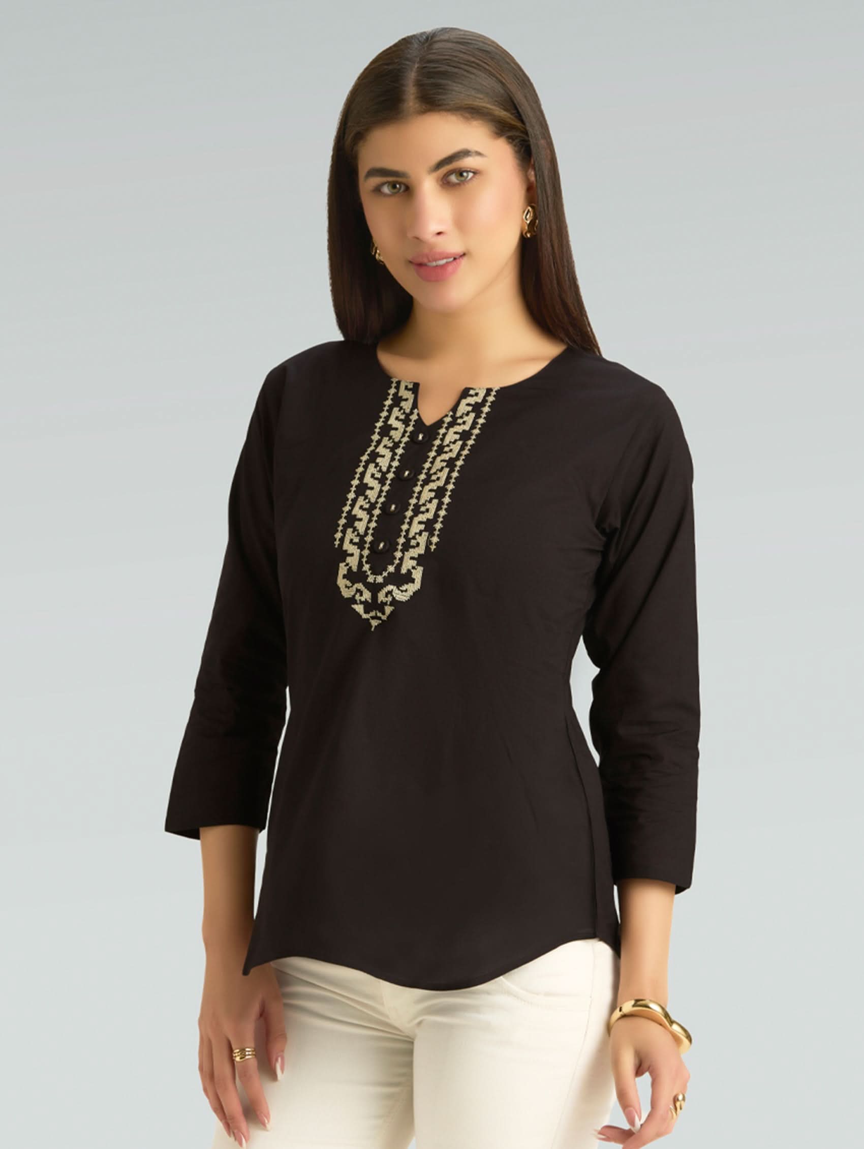 Woman wearing a black top with gold embroidery on a gray background