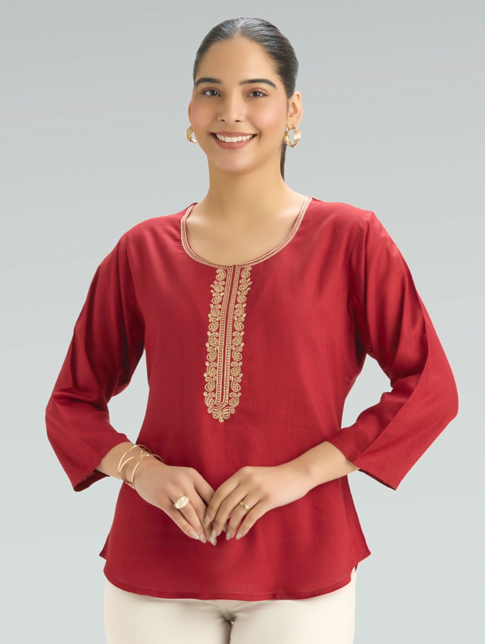 Woman wearing a red top with gold embroidery on a gray background